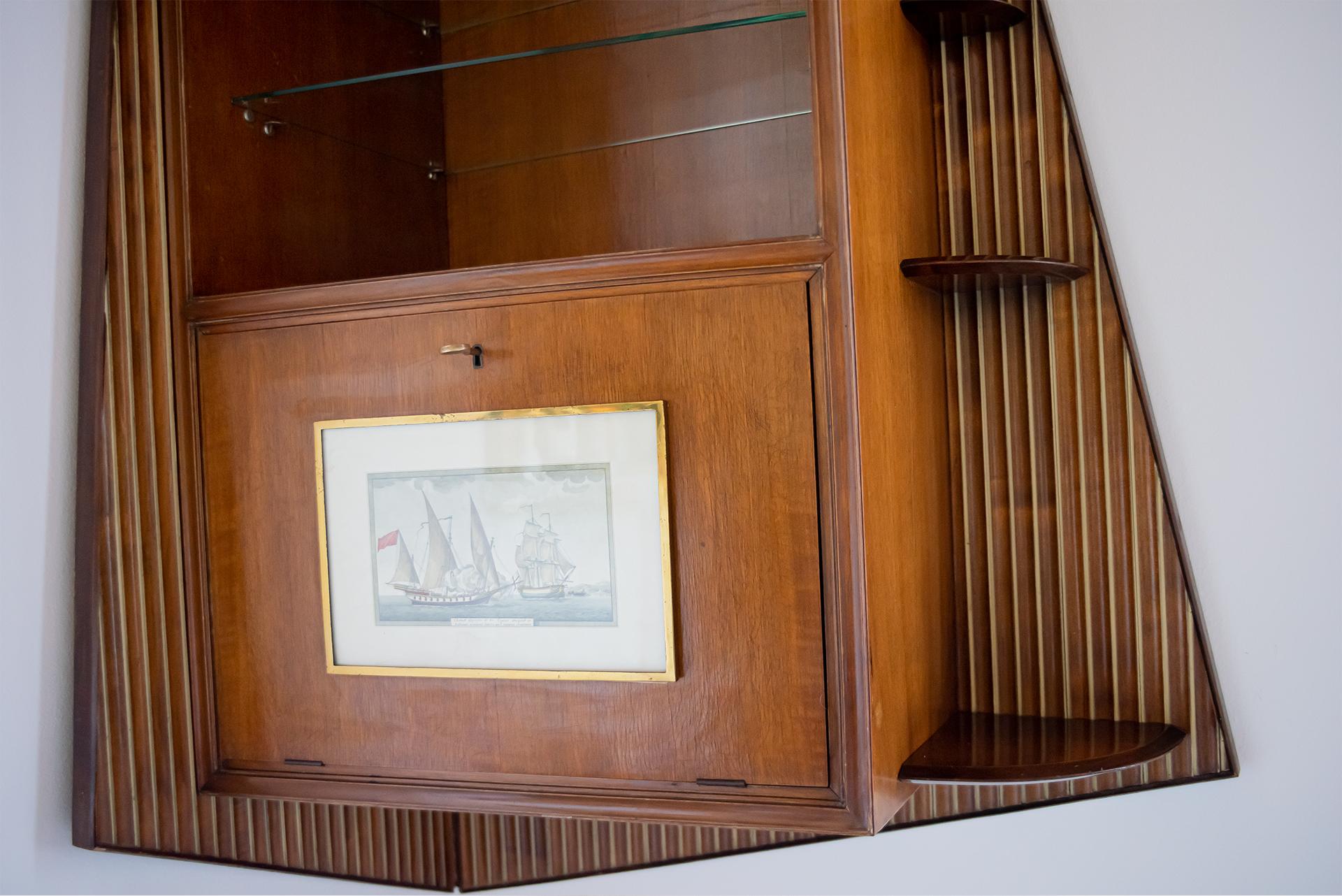 Fluted mahogany, brass details and glass shelves.
The light is electrified for European standards. Includes original key and print of the naval scene.

