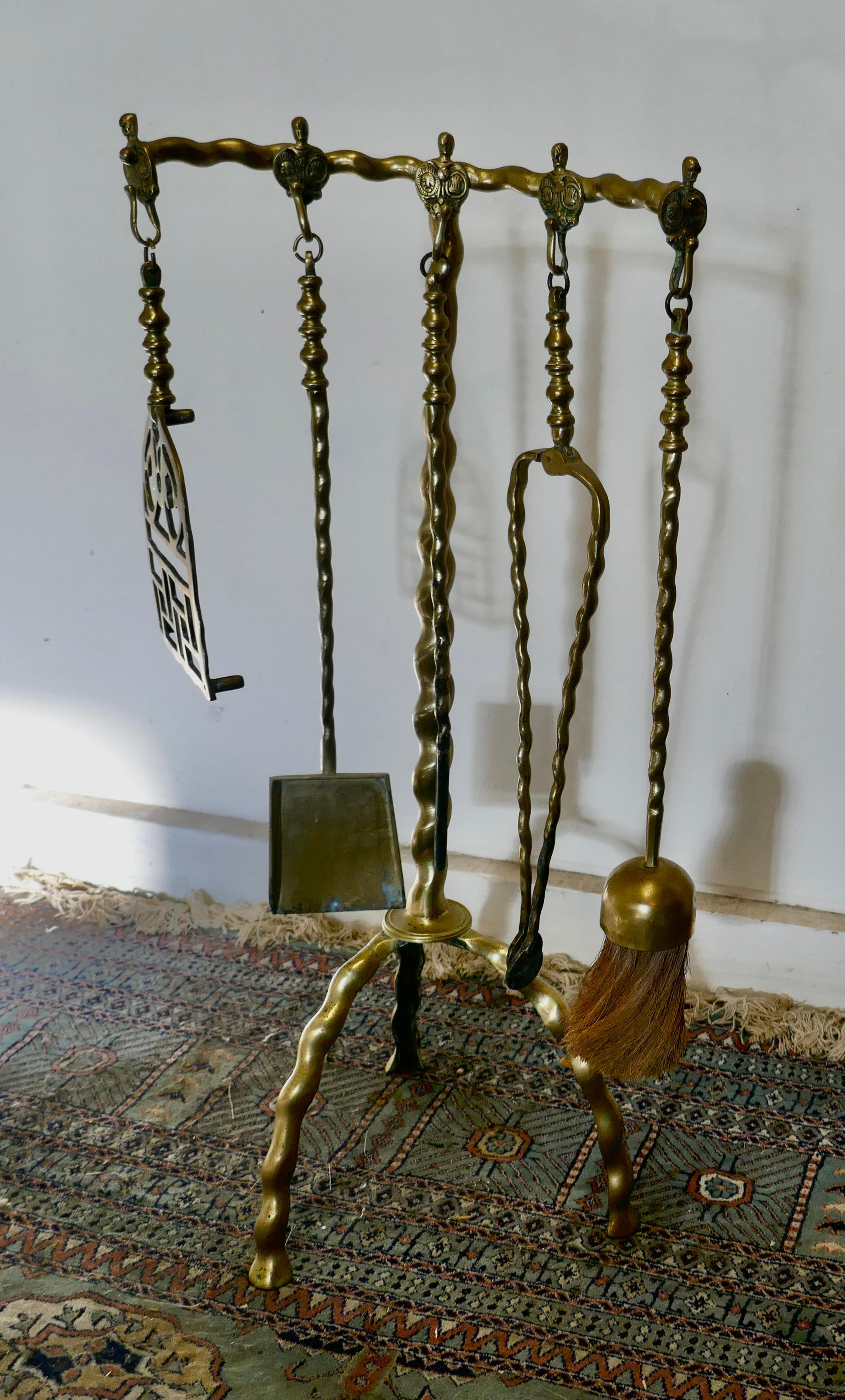 Unusual brass fireside companion set, 5 fireside tools

This is a long handled set on its own tall curved stand, shovel, tongs, brush, trivet and poker 
The stand has twisted look, and the hooks are decorated with gothic motifs
The stand 31”