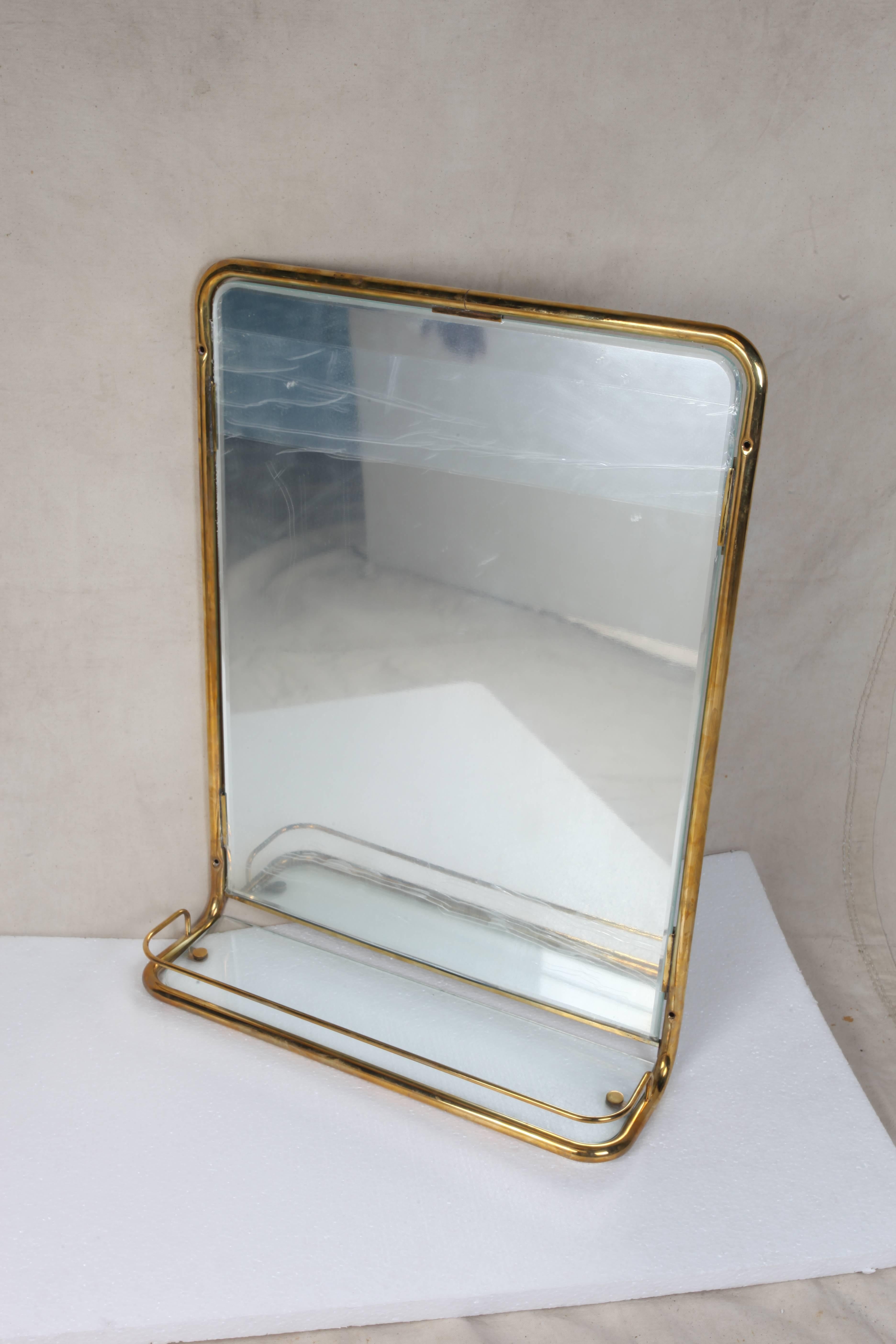 A great brass wall mirror from the stateroom of a decommissioned cruise ship. Features a new mirror and glass shelf with the original brass railing around it, circa 1960s. When found, these had been slathered with old white paint and all the glass