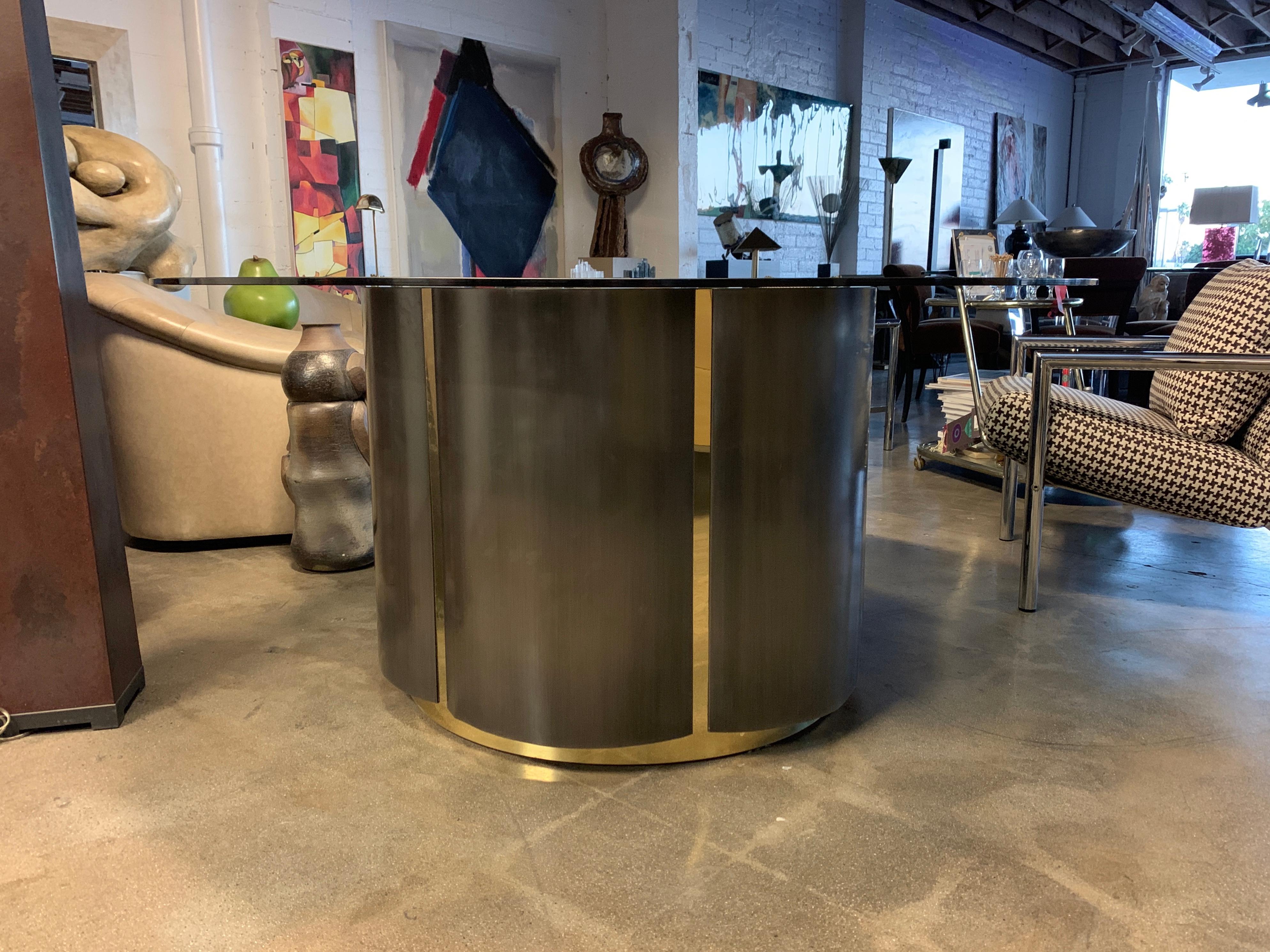 An unusual table well made with a cloverleaf shape. It is made of brushed metal and brass accents. It features a beautiful pice of smoked glass. The glass is 3/8 inch thick and 60 inches in diameter. There are some rust spots to one area pictured,