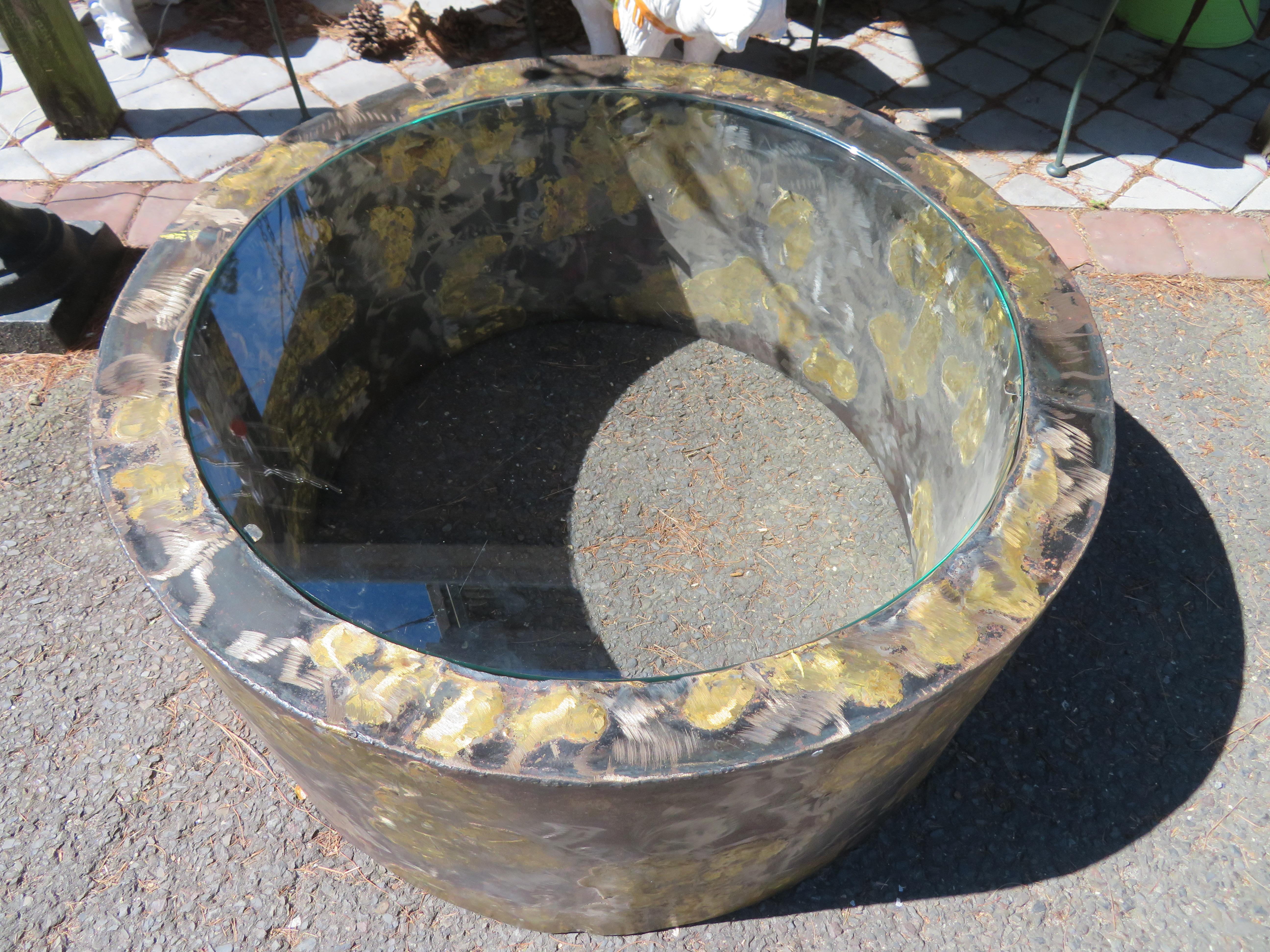 Insolite table basse brutaliste en forme de cylindre attribuée par Silas Steele en laiton et en acier.  Nous aimons la surface texturée avec l'utilisation de laiton et d'acier soudés ensemble.  Le verre affleure le plateau, ce qui confère à cette