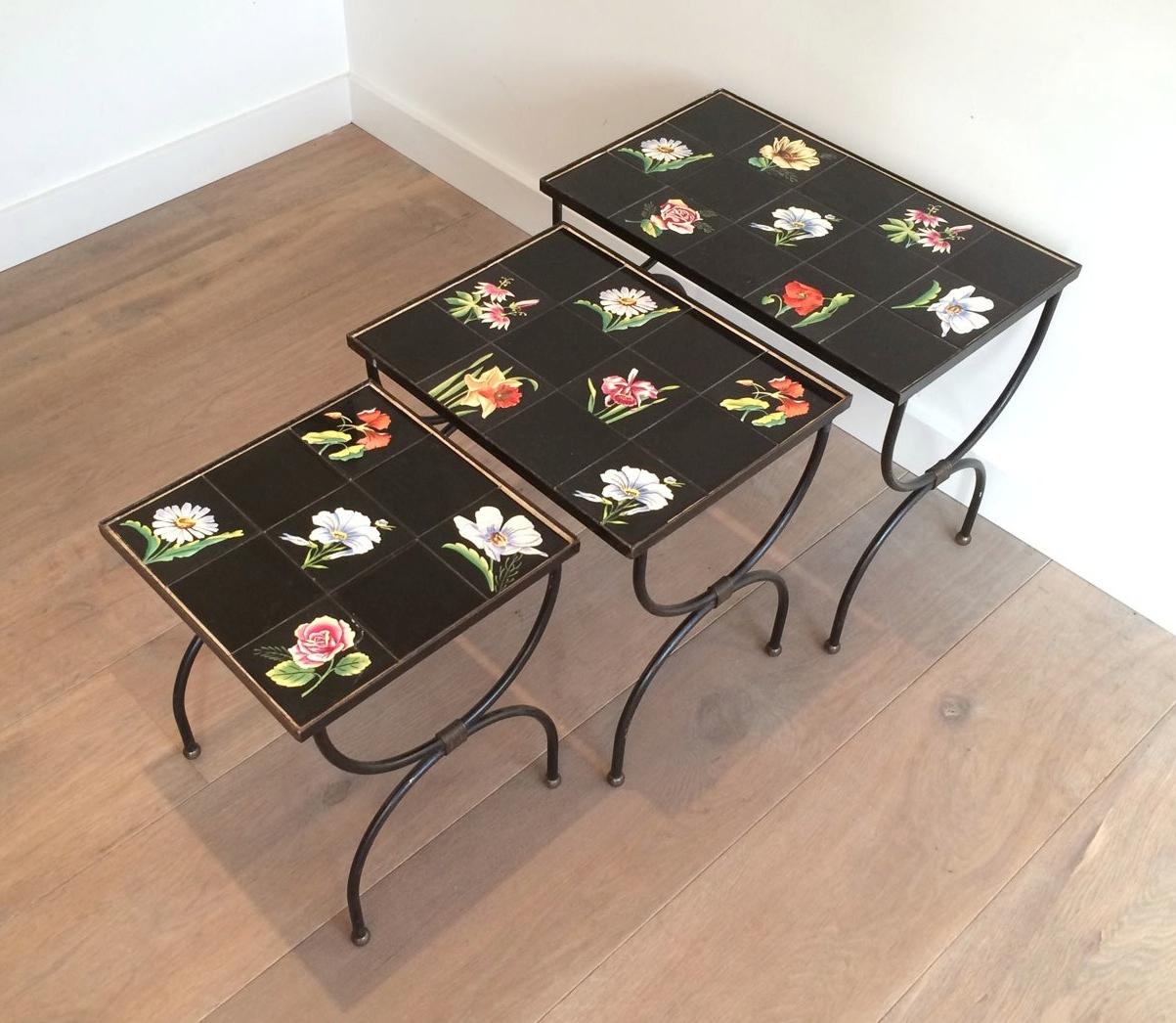 This unusual nesting tables are made of black lacquered iron with ceramic tiles on top showing flowers. This is a French Work in the style of famous French designer Jean Royère. Circa 1950.