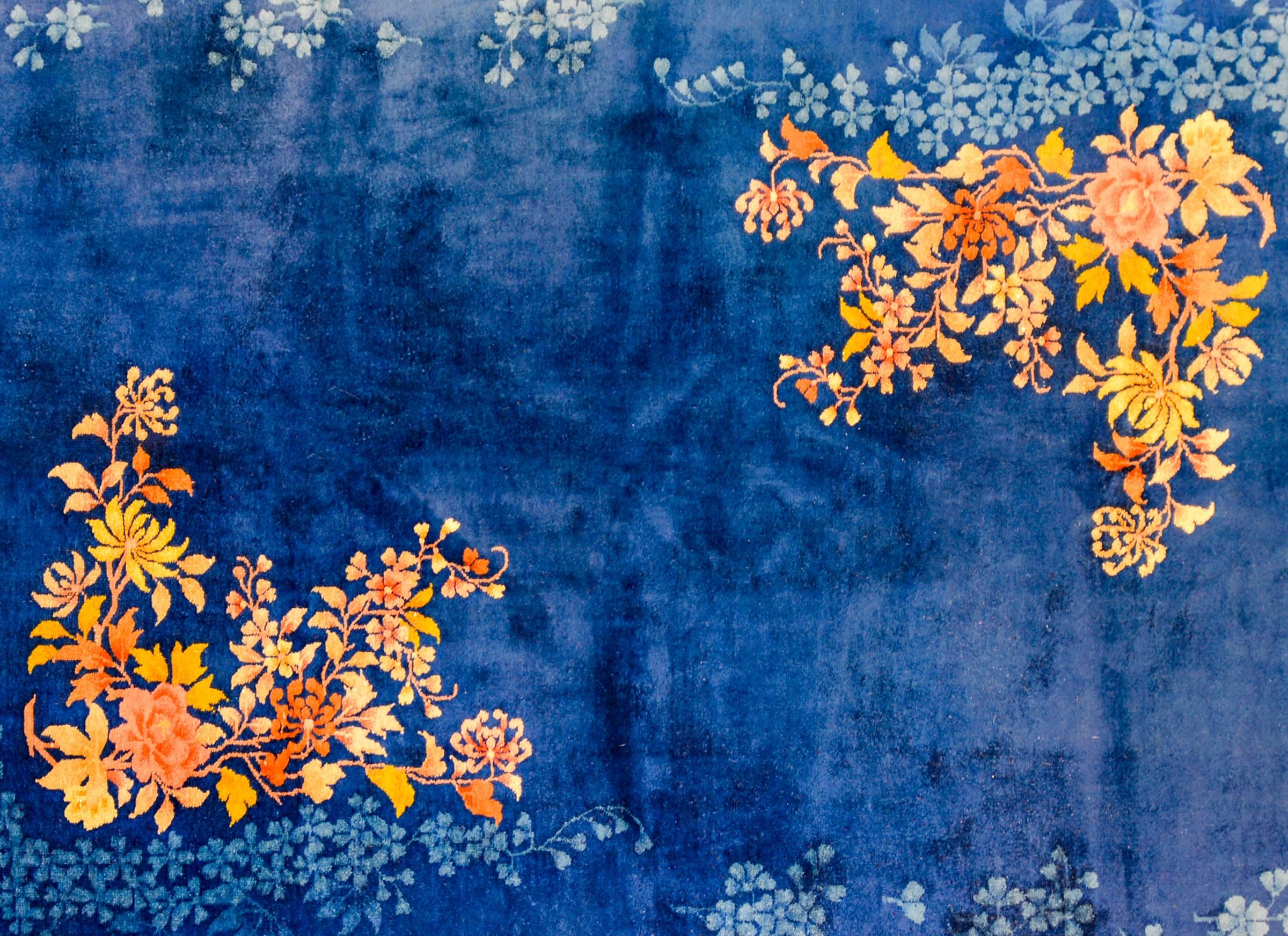 An unusual early 20th century Chinese Art Deco rug with an asymmetrical all-over multicolored flowering peony, chrysanthemum, and cherry blossom pattern woven in orange, gold, and brown vegetable dyed wool with a matching pale indigo 