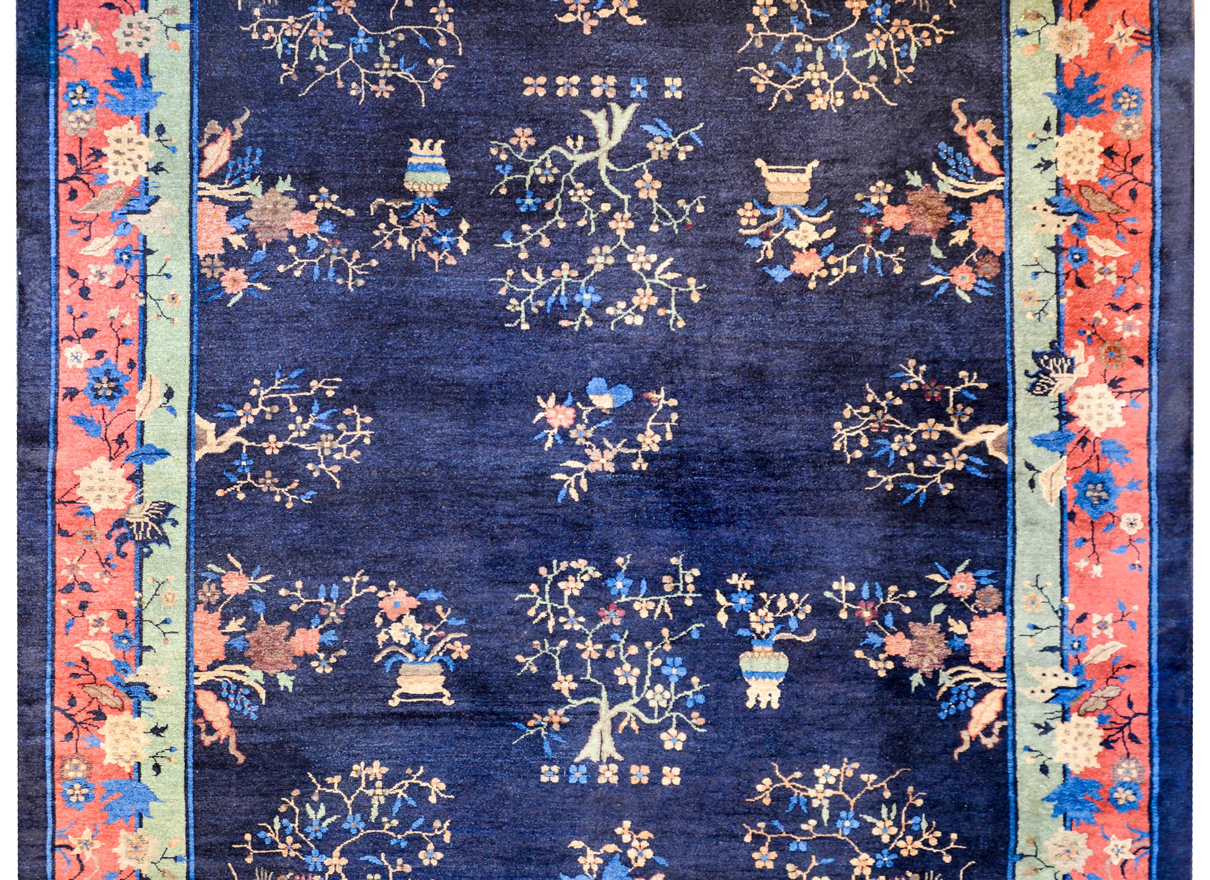 An unusual early 20th century Chinese Art Deco rug with an all-over patters of multicolored flowering trees and pots planted with peonies and other auspicious flowers, all on a dark indigo background. The border is complex with dark and light