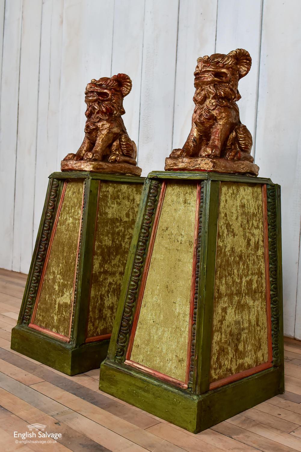 Pair of stylised temple lions or Foo dogs on plinths. The wooden plinths are covered in flocked velvet and have an egg and dart surround to each face. The composition stone lions / dogs have a gilded red coloured finish. Overall dimensions are given