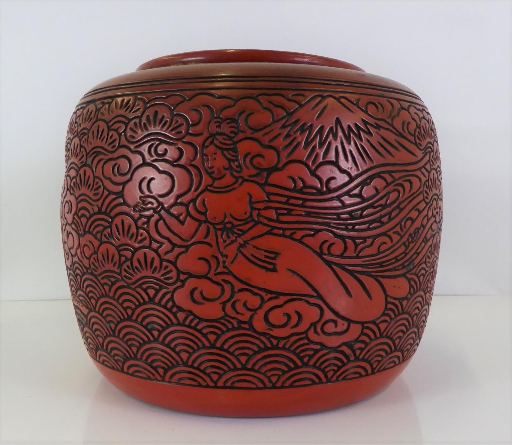 Unusual Cinnabar colored Earthenware Hibachi with cover from the Showa Period in Japan. The design is of a Deity or Goddess, possibly Ame-no-Uzume, floating among the clouds with Mt. Fuji in the distance. Ame-no-Uzume is a very positive Kami, a