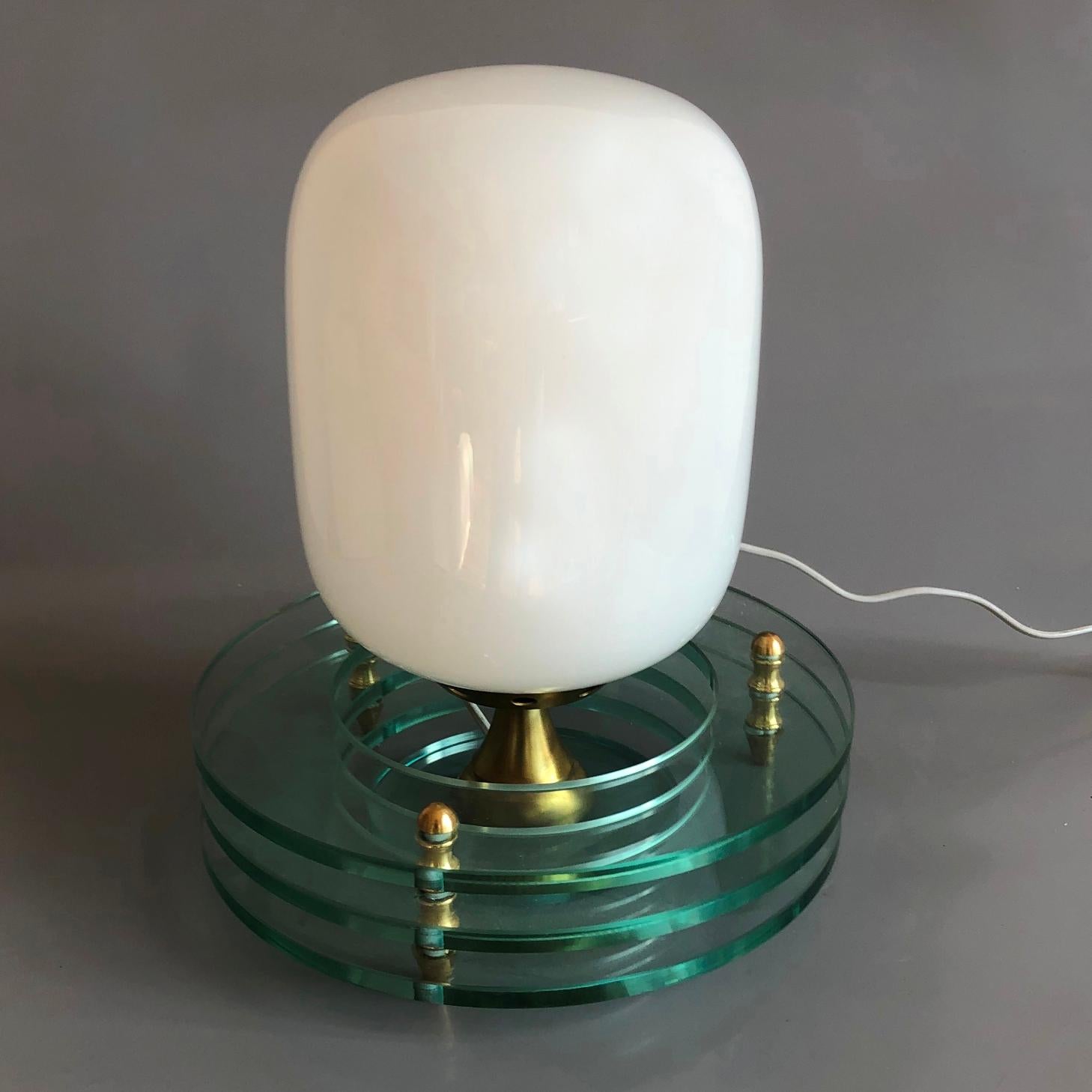 Table lamp consisting of two parts. Cocoon shaped opaline glass shade and triple ringed green base with brass fitting elements.
Original condition. All original pieces.