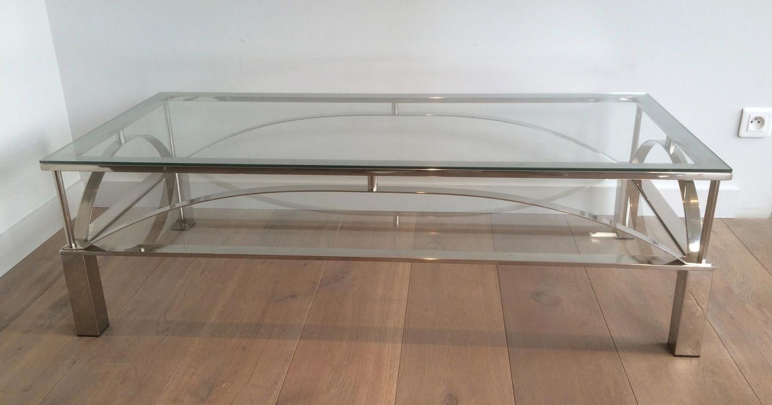 This unusual coffee table is made of chrome with 2 glass shelves. It has curved chromed metal parts on each side of the table. This is a French work. Circa 1960.
