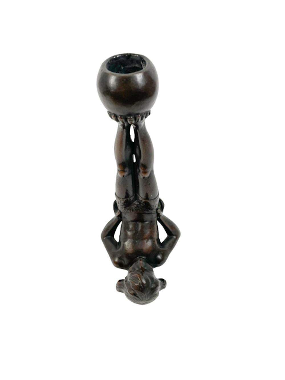 Unusual early 20th century patinated copper figural candlestick in the form of a boy wearing gym shorts and standing on his shoulders propped up by his arms and with his feet in the air holding an exercise ball. 