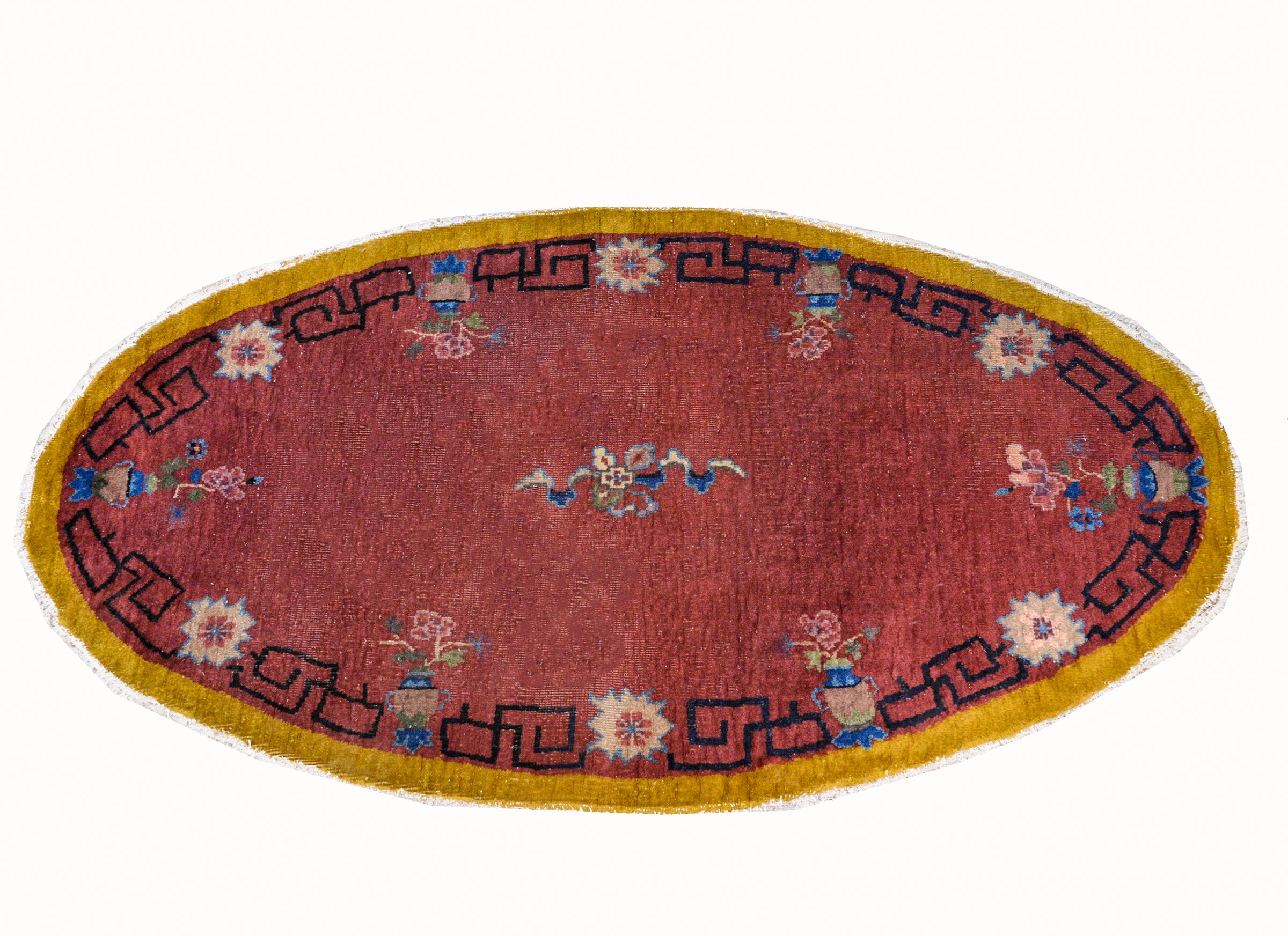 An unusual early 20th century oval Chinese Art Deco rug with a cranberry center, surrounded by a meandering motif and floral patterned border, with an outer gold stripe border.