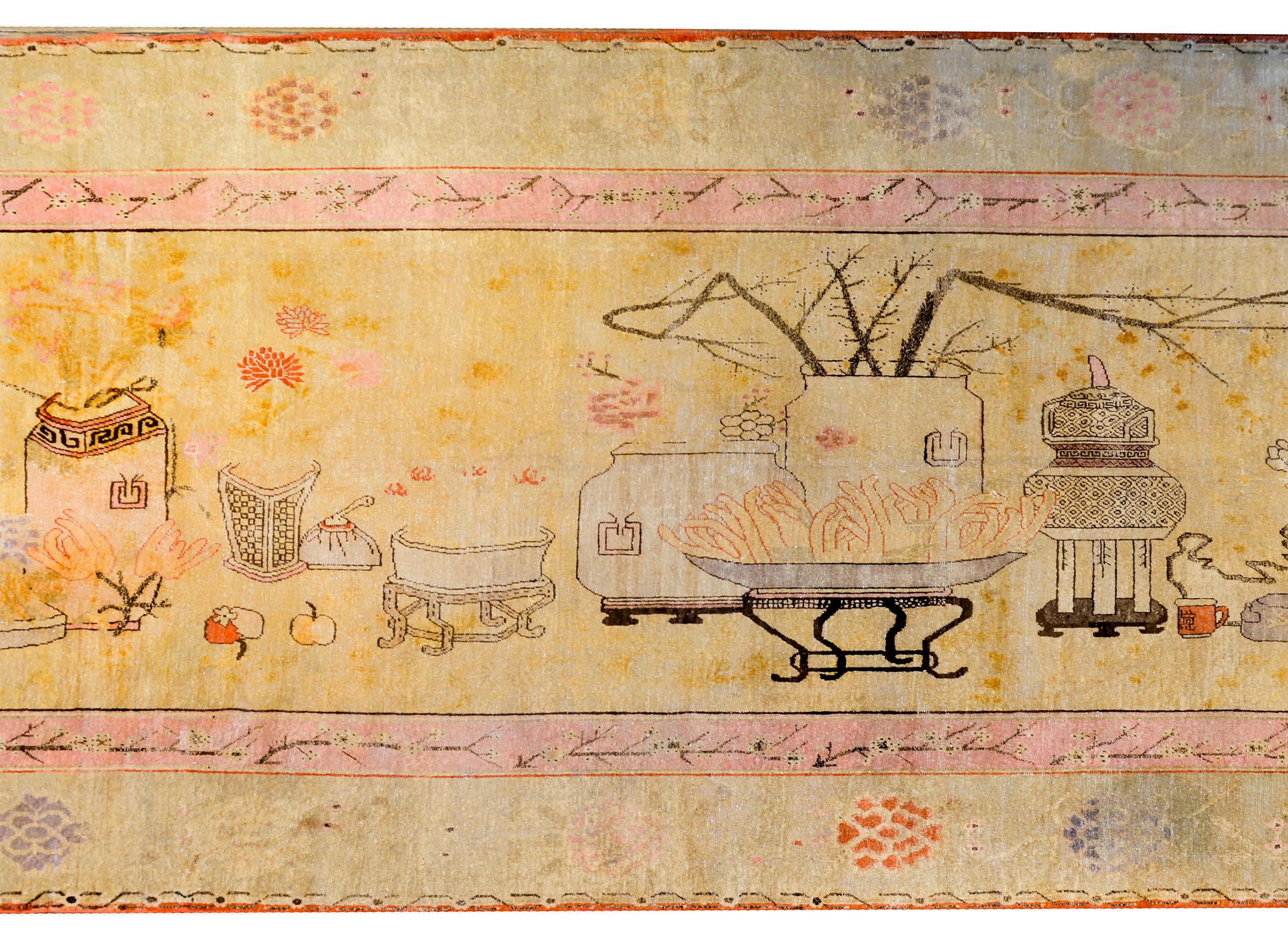 An unusual early 20th century Central Asian pictorial Khotan rug with a still-life image depicting myriad scholar's objects including potted peonies, chrysanthemum, and cherry blossoms, incense burners, Buddha's fingers, peaches, and scholar's