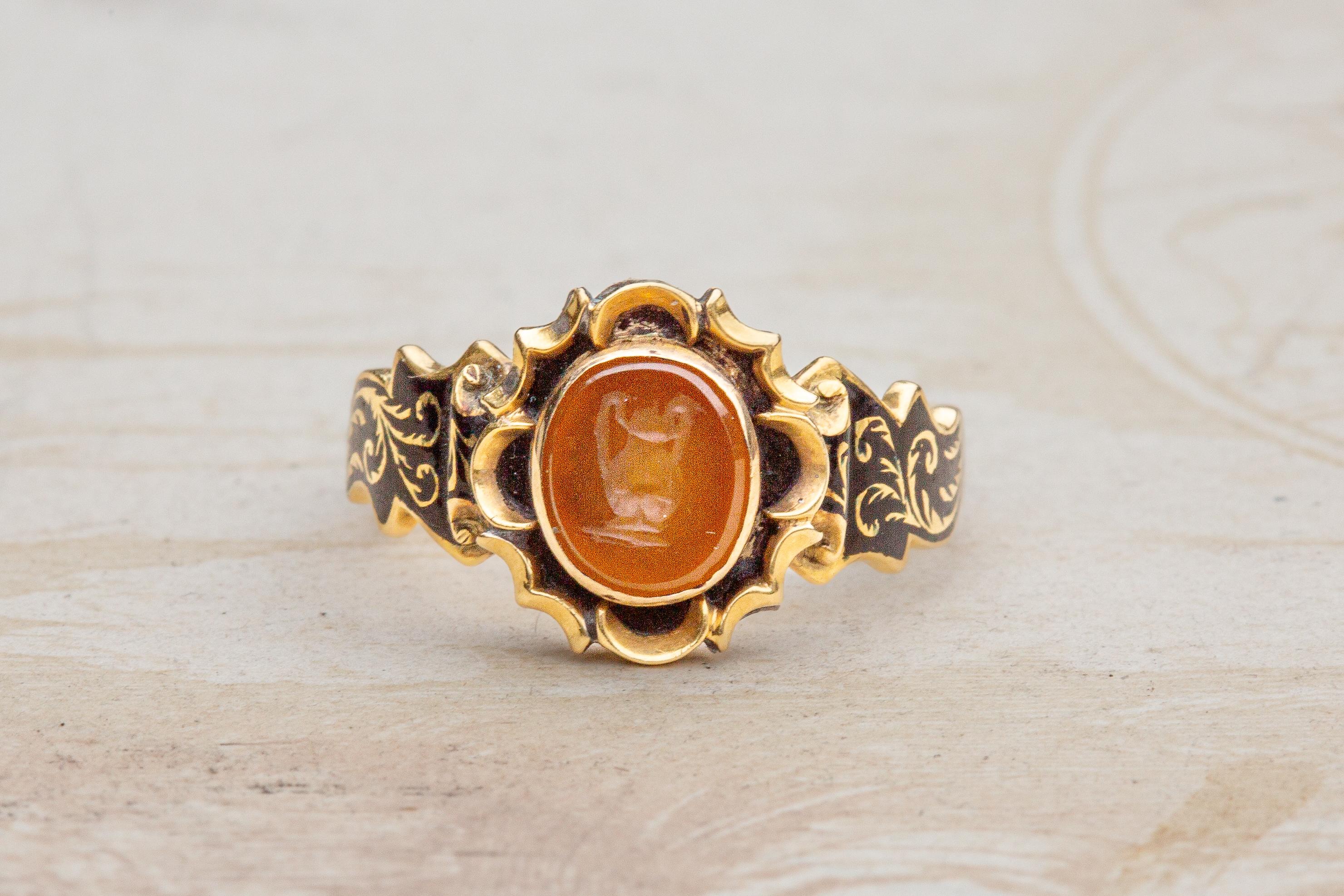 This unusual mourning ring was made in London during the early Victorian period, circa 1849. The centrepiece of this unusual mourning is an orange agate stone, engraved with an urn in neoclassical style. The intaglio is surrounded by a gothic