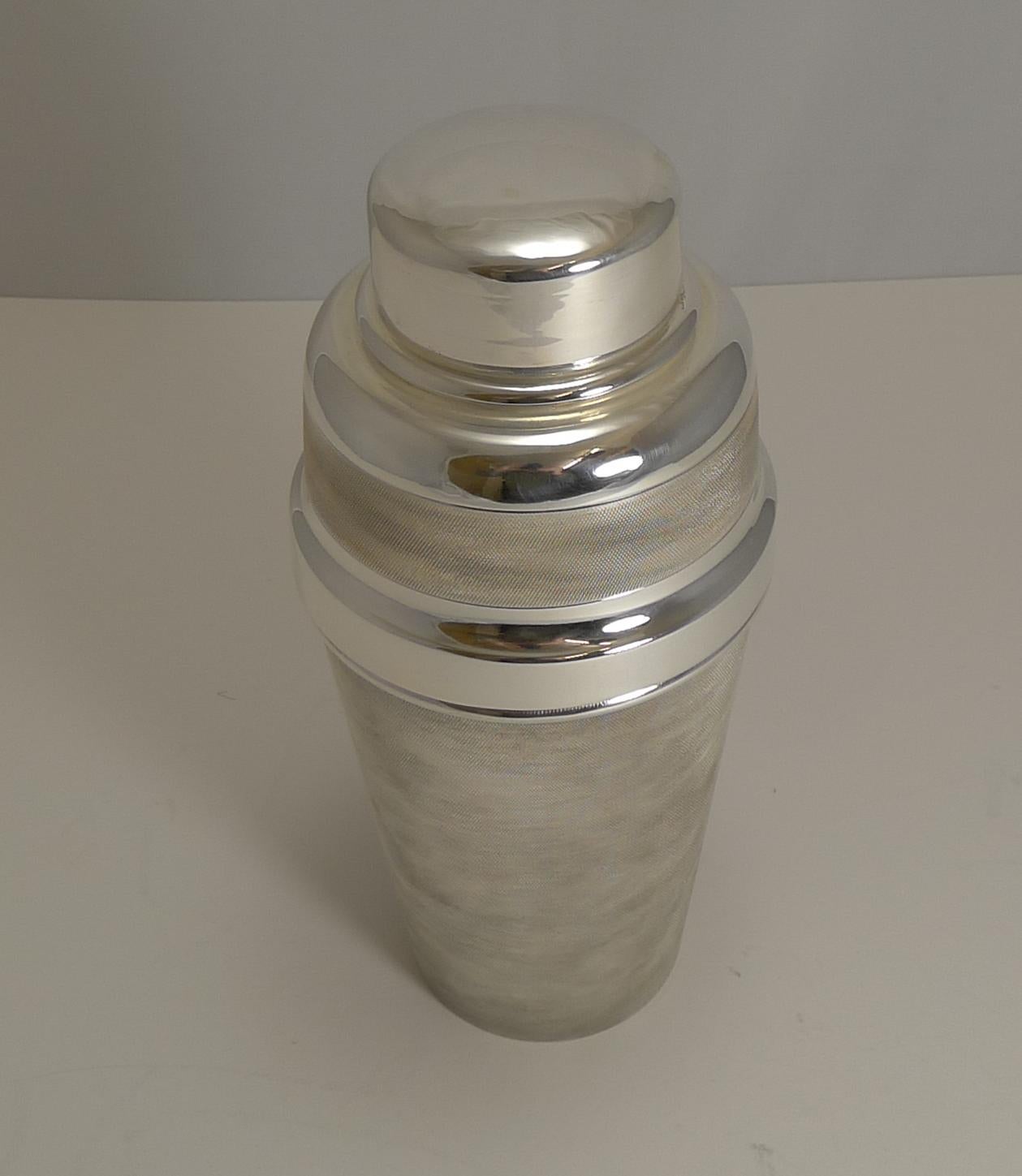 A fabulous and unusual English silver plated cocktail shaker with the body having a deep engine turned decoration creating a good textured area to securely hold and having a wonderful tactile finish.

The underside isn't marked by the maker but