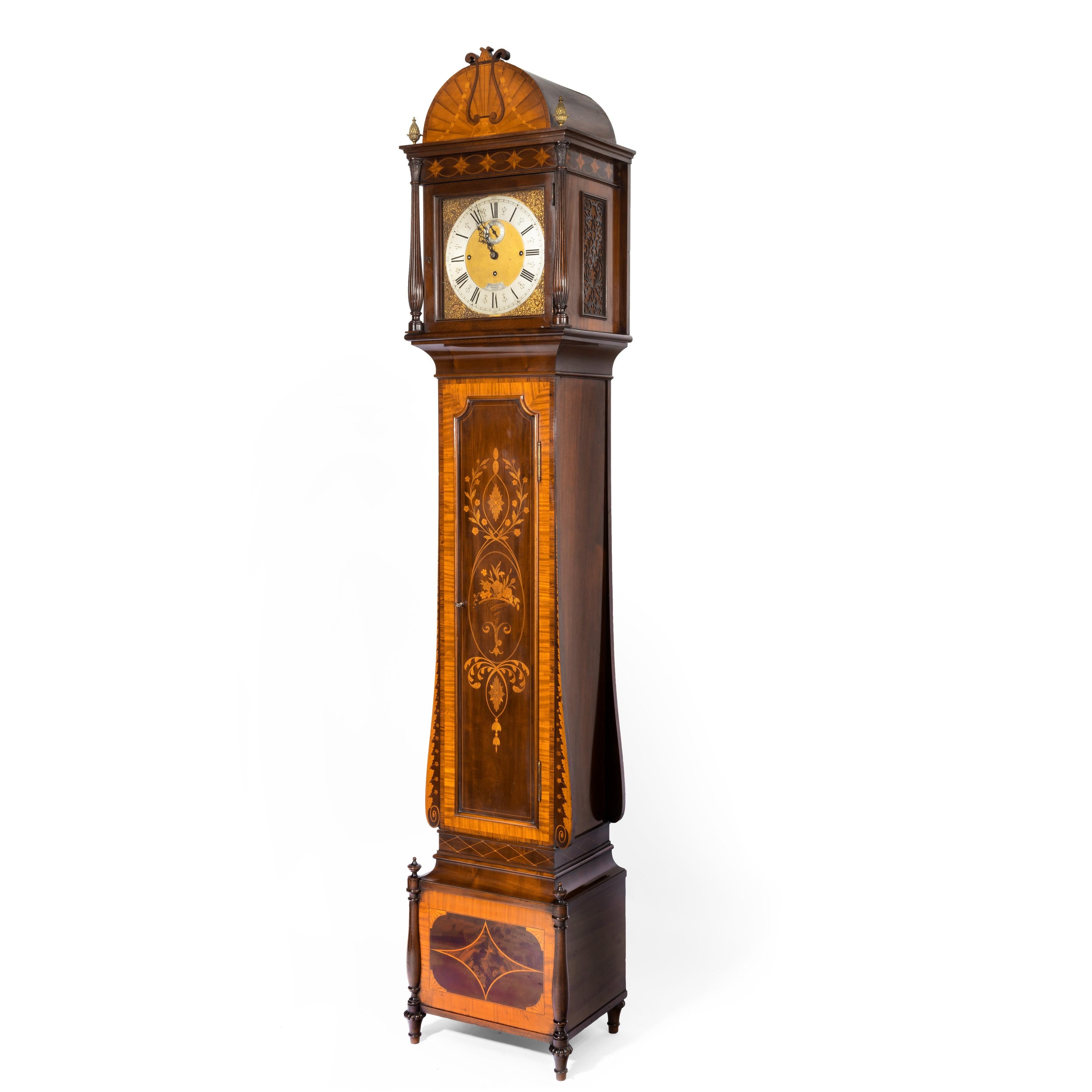 An unusual flame mahogany long-case clock attributed to Maples with a Smith & Sons 3-train movement, the case with a stepped base, the hood with two fluted columns and brass finials surmounted by a hemi-spherical crest decorated with a lyre against