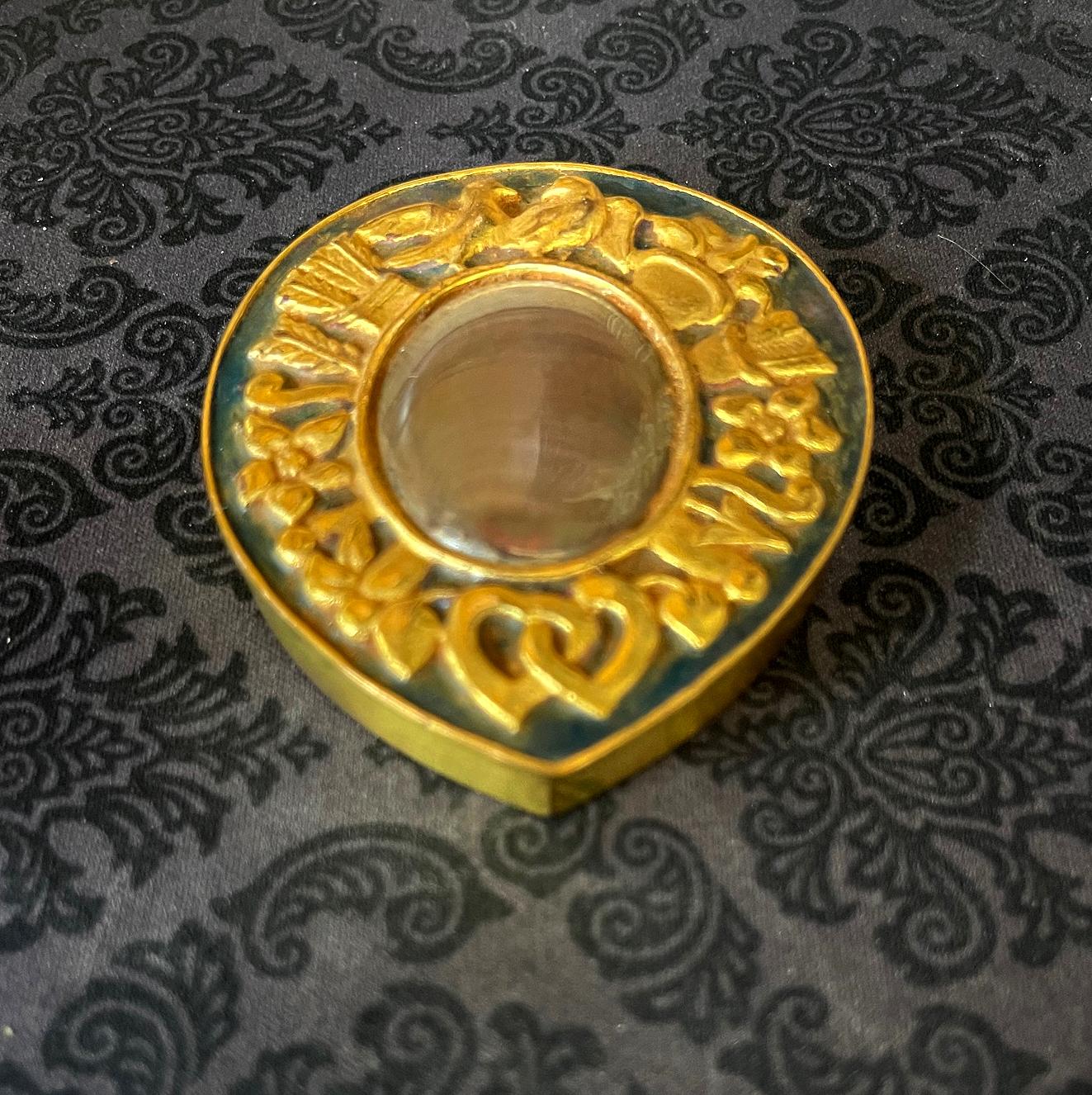 A cast bronze box used as a poudrier (powder box) by French Parisian Art Jeweler Line Vautrin (1913-1997) circa 1950s. The lidded box is in a form a tear drop and features a relief band of motif including two kissing pigeons, arrows tails and heads