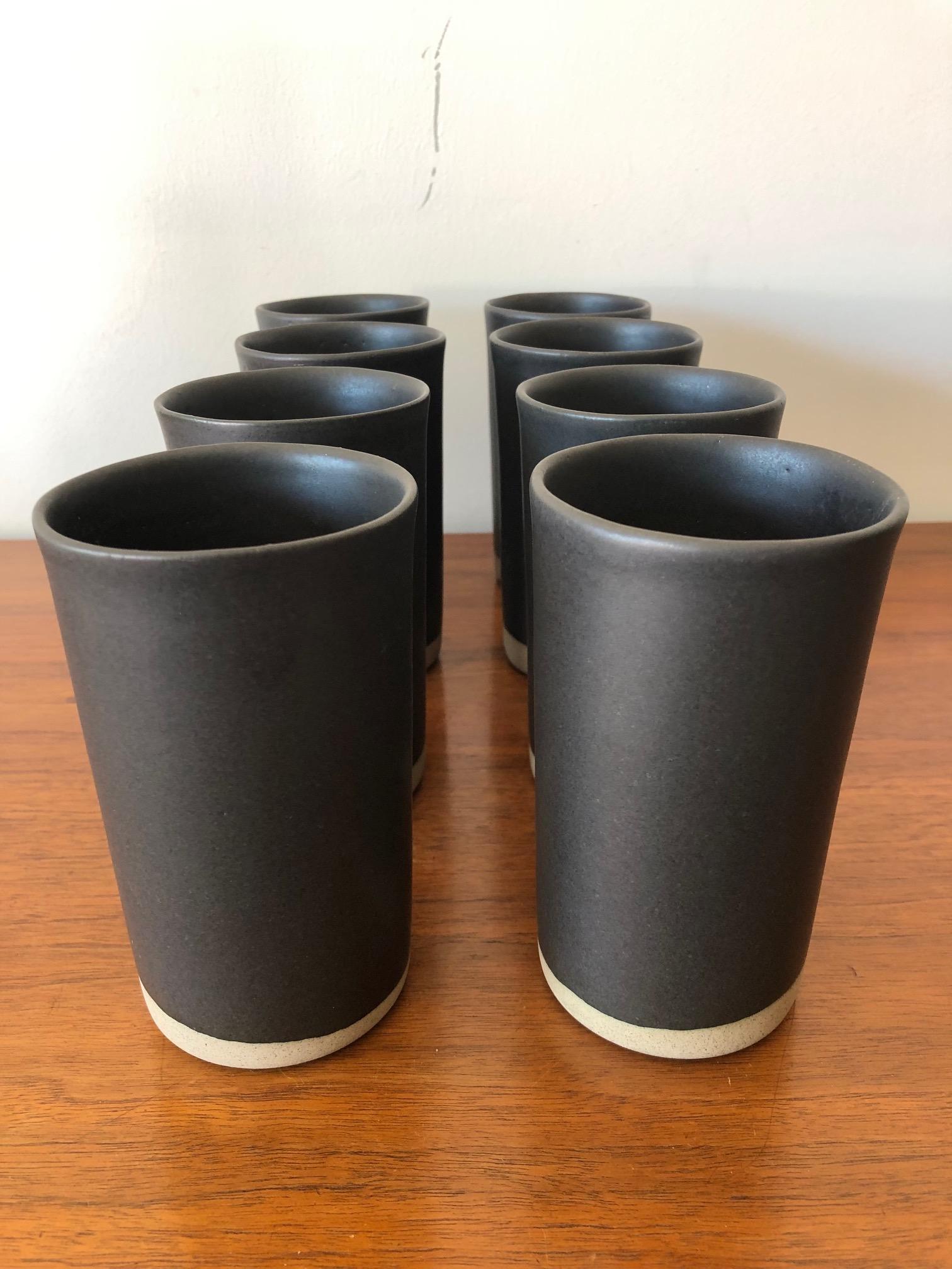 An interesting set of eight (8) ceramic cups by Gordon Martz, circa 1960s. Elegant simple form in dark espresso brown-almost black with contrasting raw natural surface on the bottom. Handmade and each slightly irregular. Measuring approx. 5.5