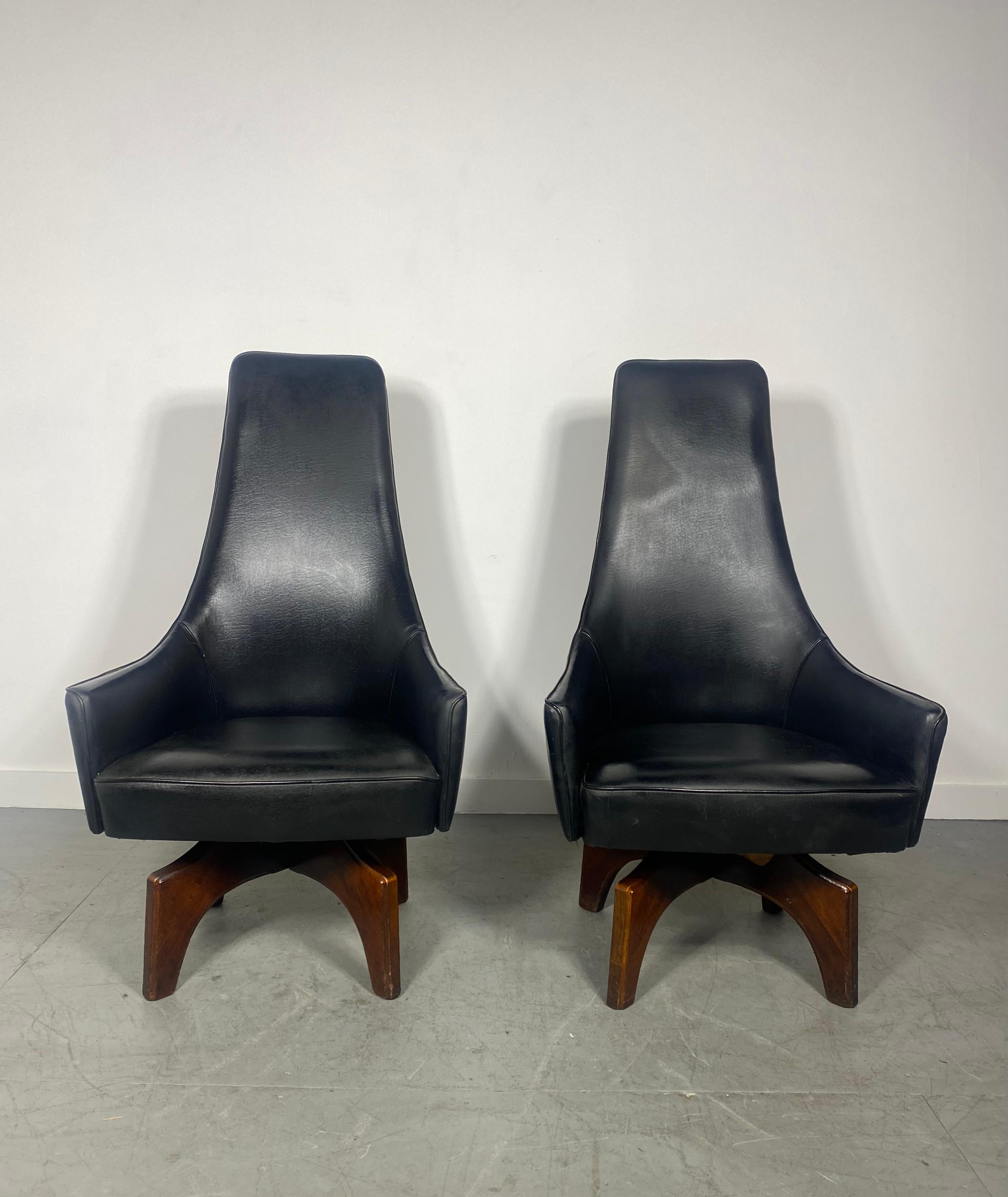 Unusual High Back Swivel Arm Chairs by Virtue Bros..Possibly designed by Adrian Pearsall ? 380% swivel,,, extremely comfortable..Stylized walnut bases.. Embossed leather shield design to backs.Classic 1950s ,60s design..Would make amazing captains