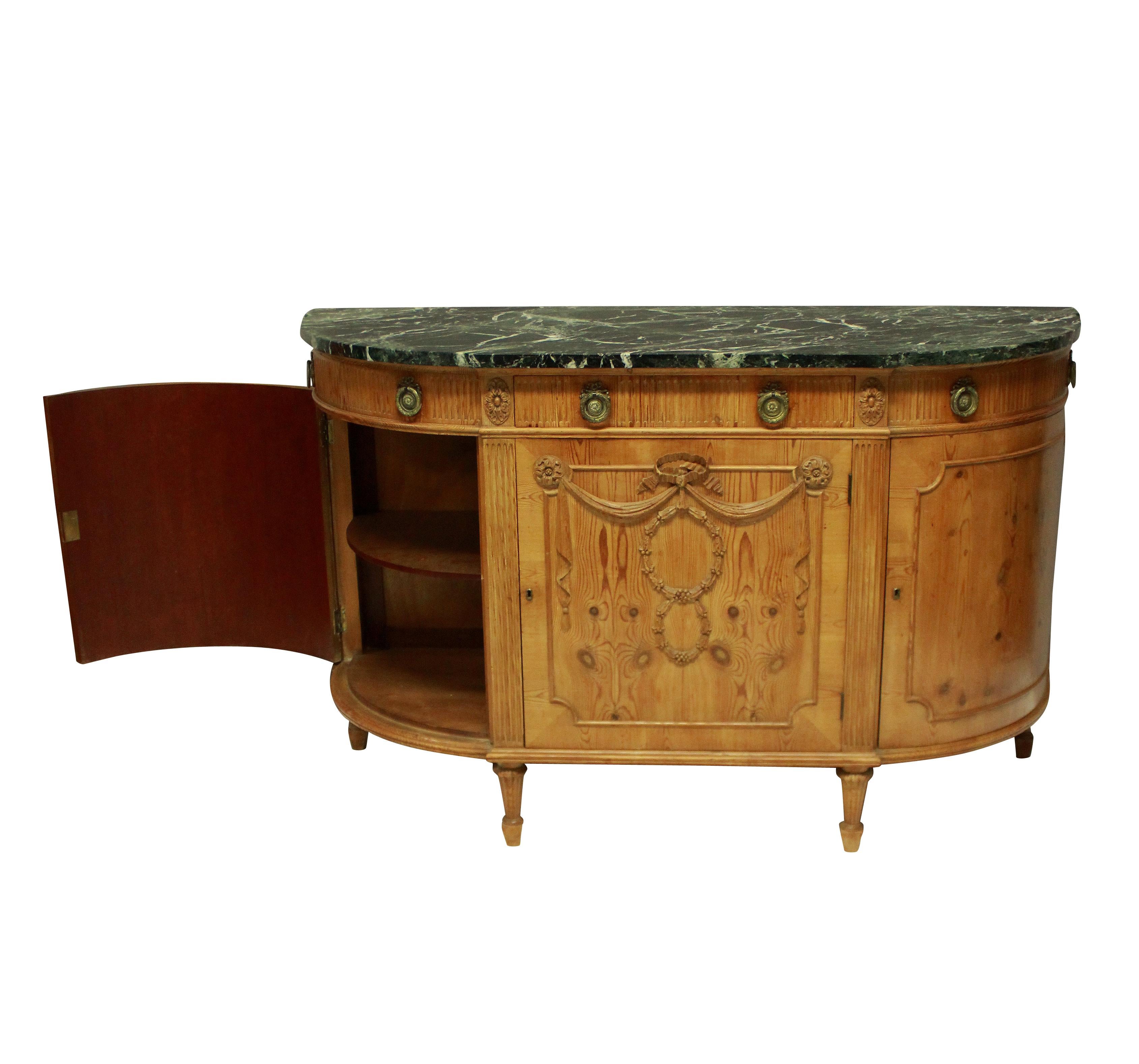 An unusual Northern French Louis XVI style demilune commode of generous proportions in carved pine. With a central cupboard and drawer, two side cupboards with dummy drawers, each with one shelf. The shaped top of antico Verdi marble.