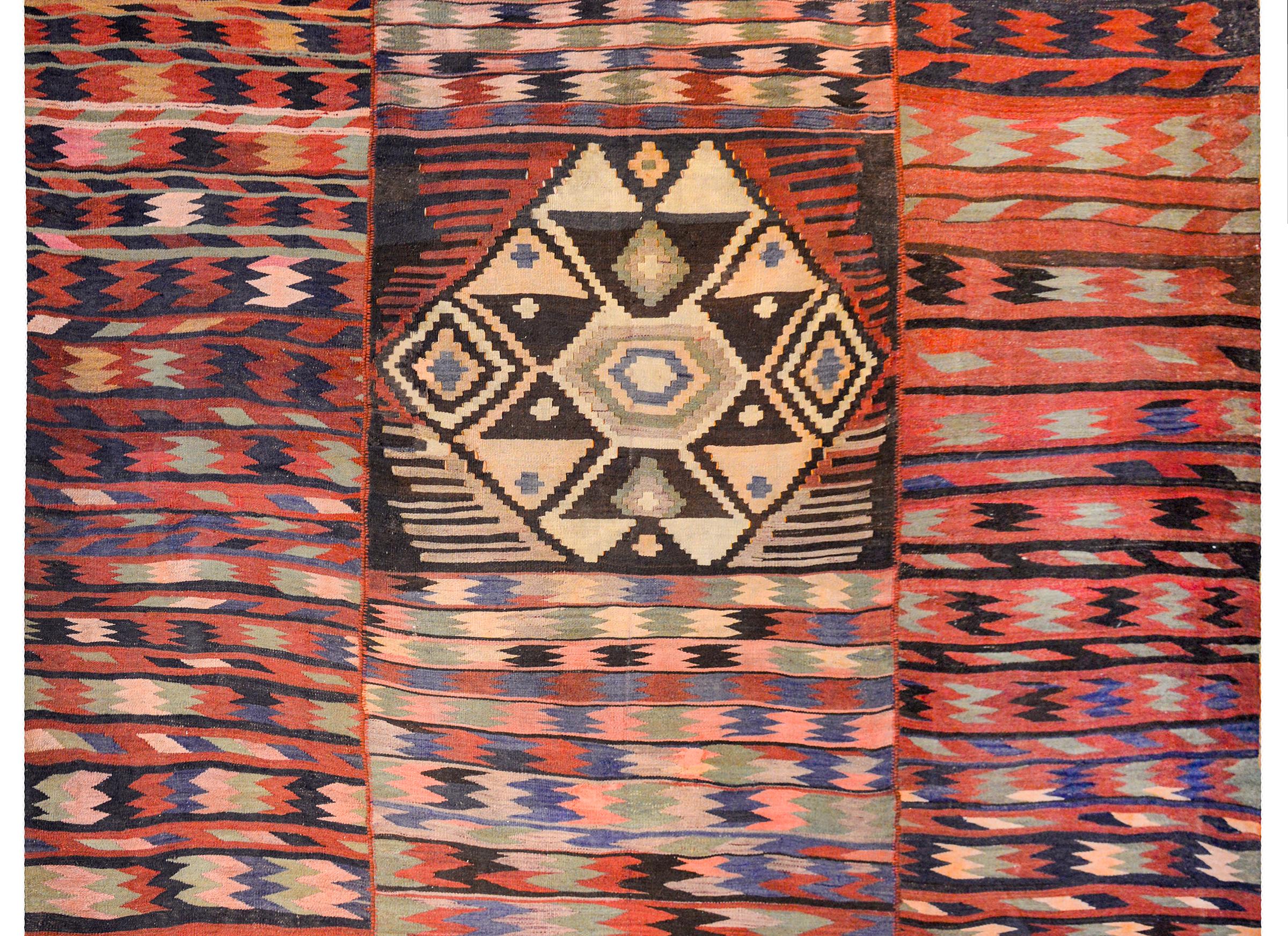An unusual mid-20th century Persian Kirmanshah kilim rug with a beautiful all-over multi-colored zigzag pattern woven in three narrow strips combined to create a larger rug. A large hexagonal medallion lies in the center, created from multiple