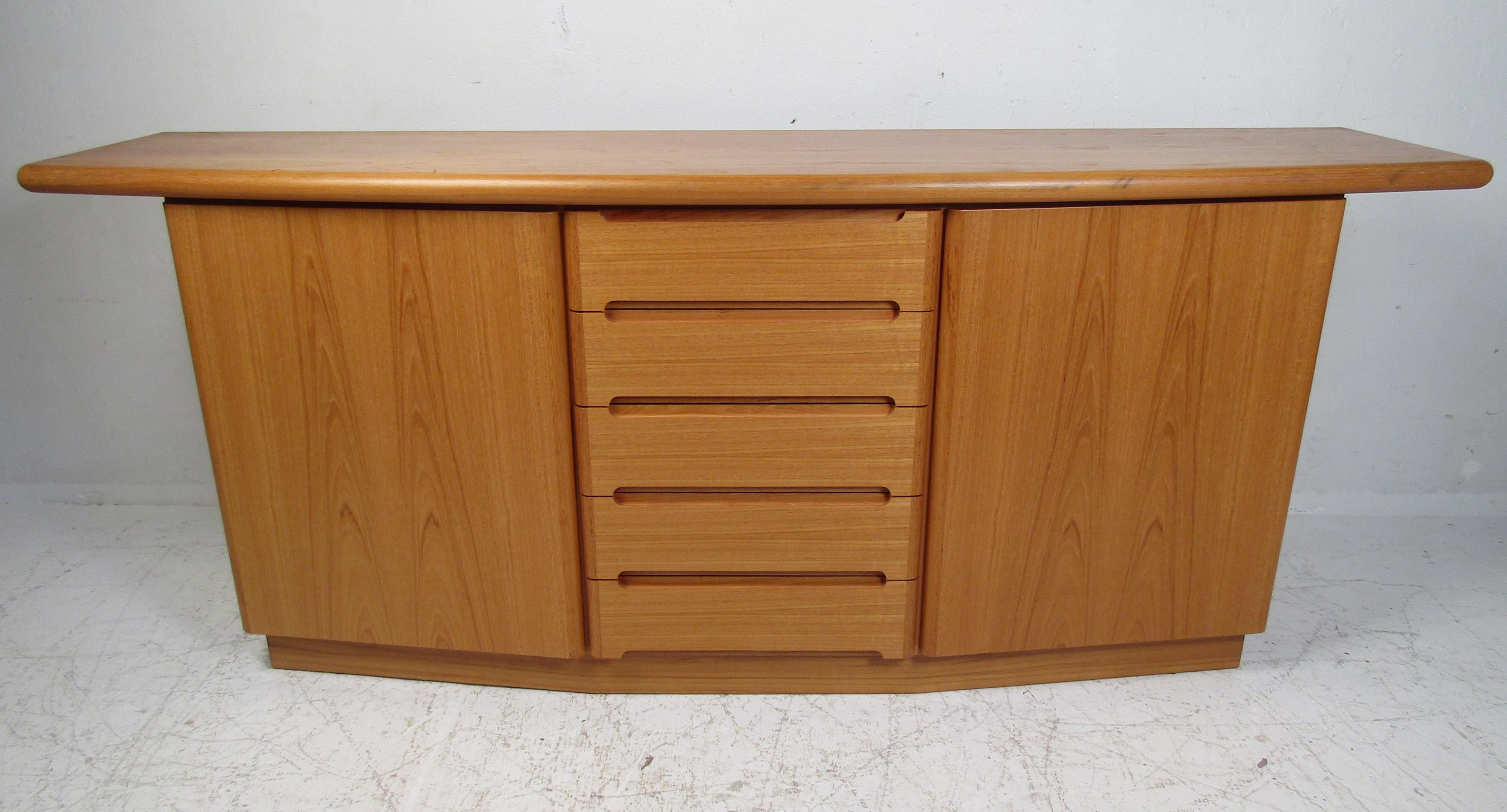 This beautiful vintage Danish server features an overhanging top with a curved front and a rich teak finish. A unique design that offers plenty of room for storage within its hefty drawers and large storage compartments. This stylish case piece