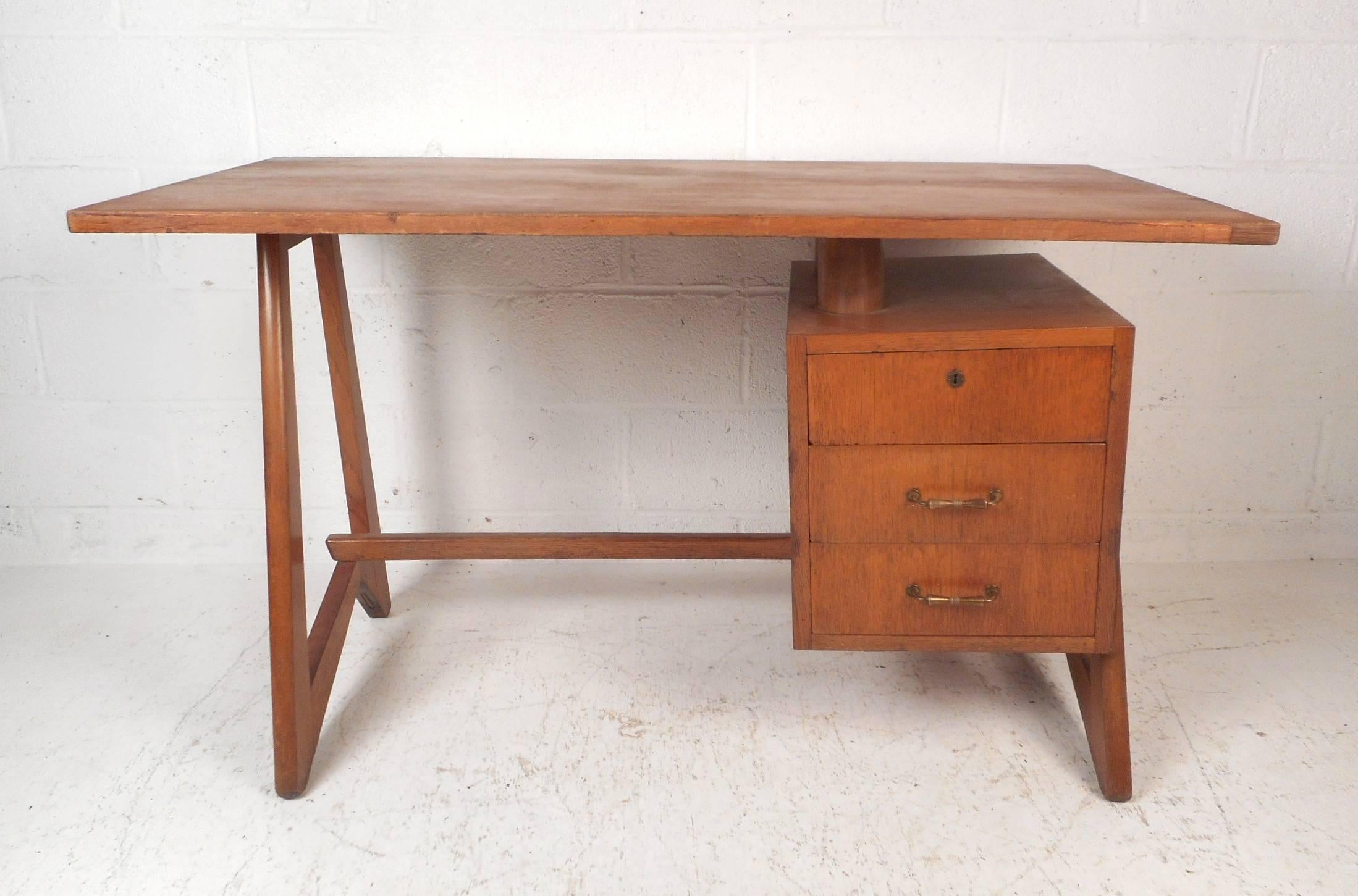 This amazing vintage modern desk features unique angled legs and a floating style table top. A beautiful case piece with a curved top, a finished back, and sculpted brass drawer pulls. This one of a kind mid-century desk offers plenty of work space