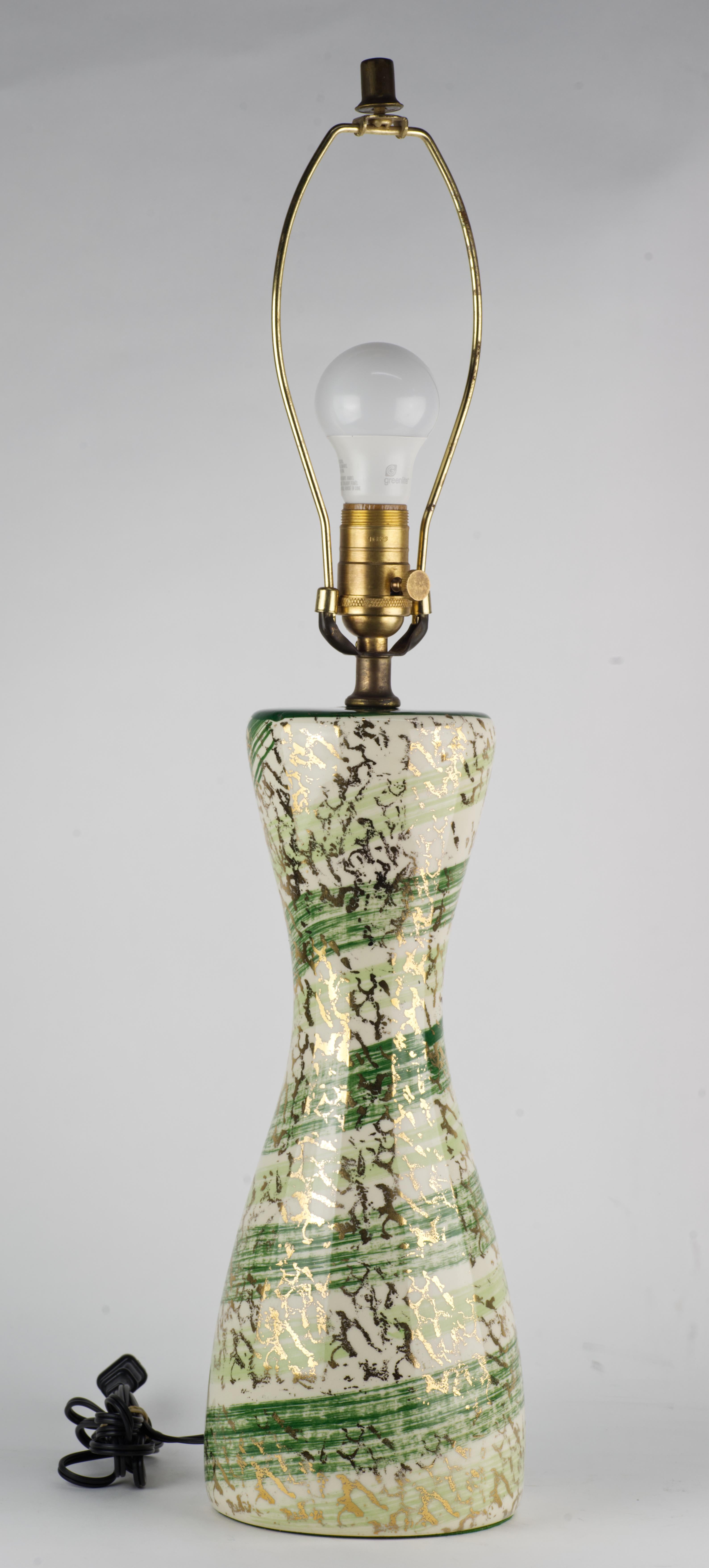  Unusual Mid Century Modern ceramic table lamp in hourglass shape is decorated with graphic gold splatter and green stripes on white background. The top part of the lamp's body is done in monochromatic deep forest green shade, creating a contrast