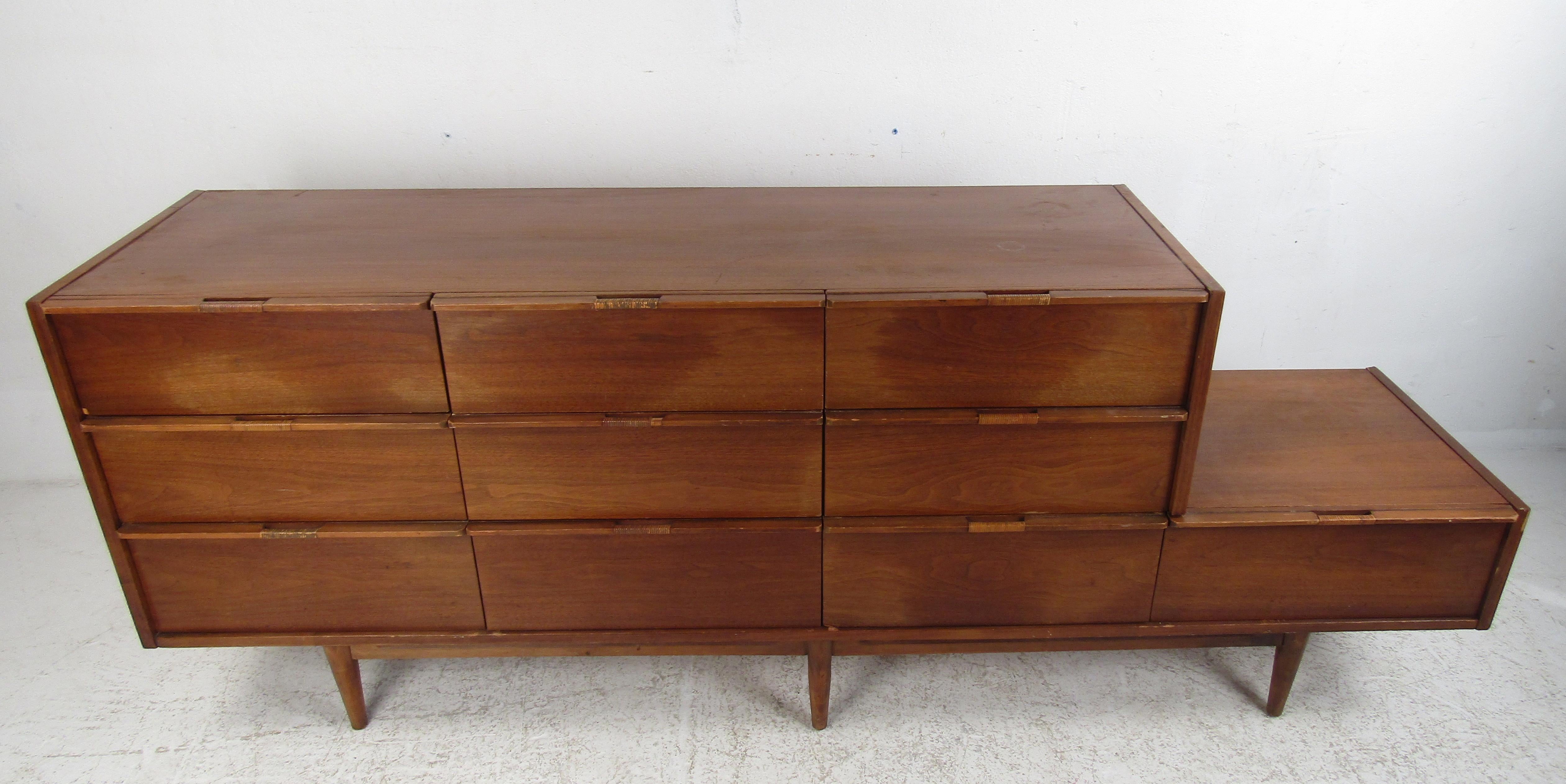 This unique vintage modern dresser boasts a step-side design with an additional drawer on the right side. A sleek case piece with ten hefty drawers ensuring plenty of room for storage. The beautiful woven drawer pulls and a charming vintage walnut