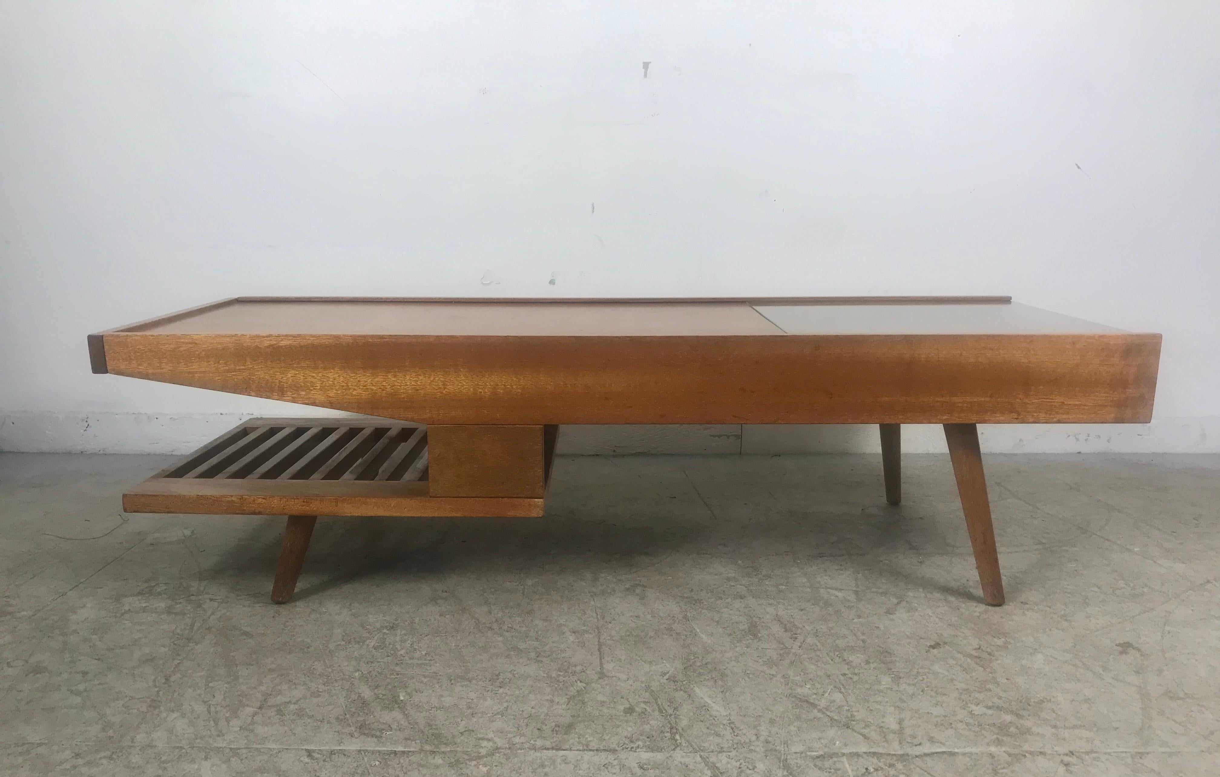 This unique mahogany coffee table designed by John Keal for Brown Saltman Co. of California circa 1950s features a sliding wood top that opens to reveal a center storage area. Retains its original coffee warmer (see photo) Also featured is a slatted