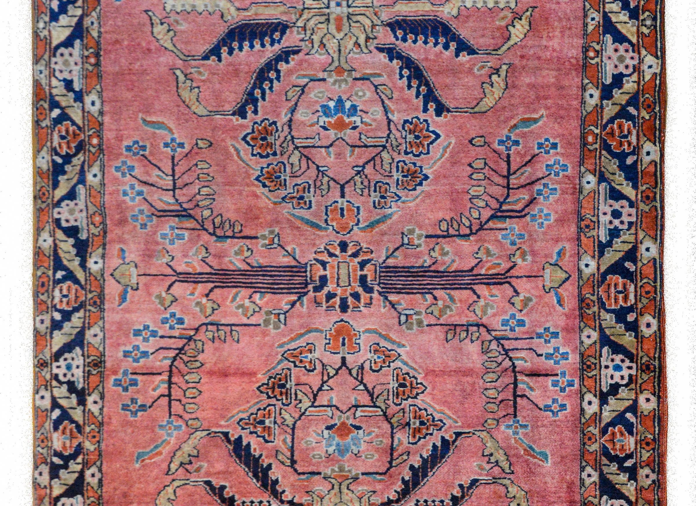 An unusual early 20th century Persian Mohajeran Sarouk rug with a striking mirrored floral pattern woven in light and dark indigo, coral, pale green, and tan wool, against a beautiful salmon colored background. The border is wonderful with a central