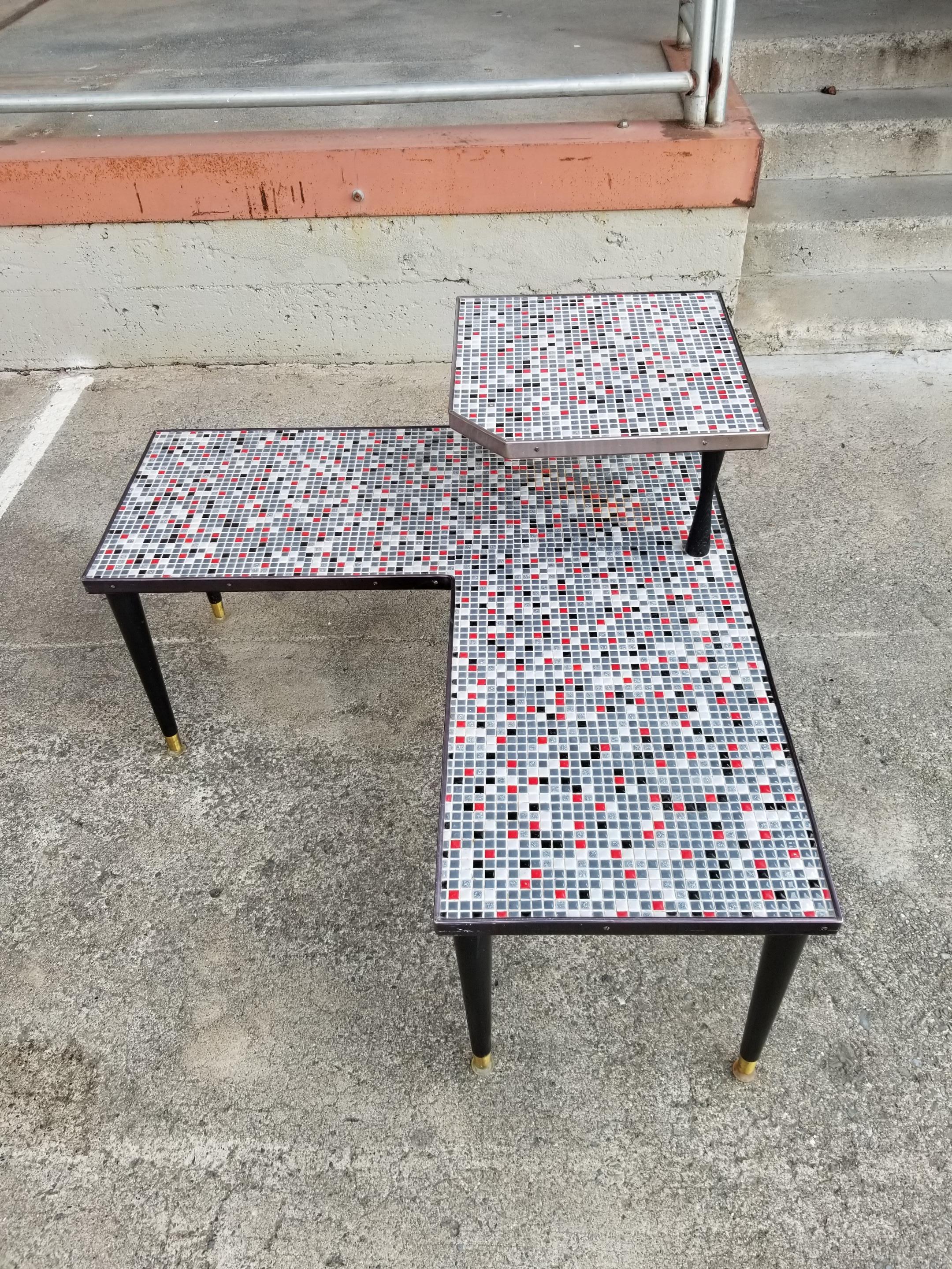 Very unusual two-tier mosaic tile corner table. Classic tapered peg legs construction, steel banded edges and hourglass post at upper tier table top. Nice brass cap plates at feet with all original glides intact. Multi-color square tiles in red,