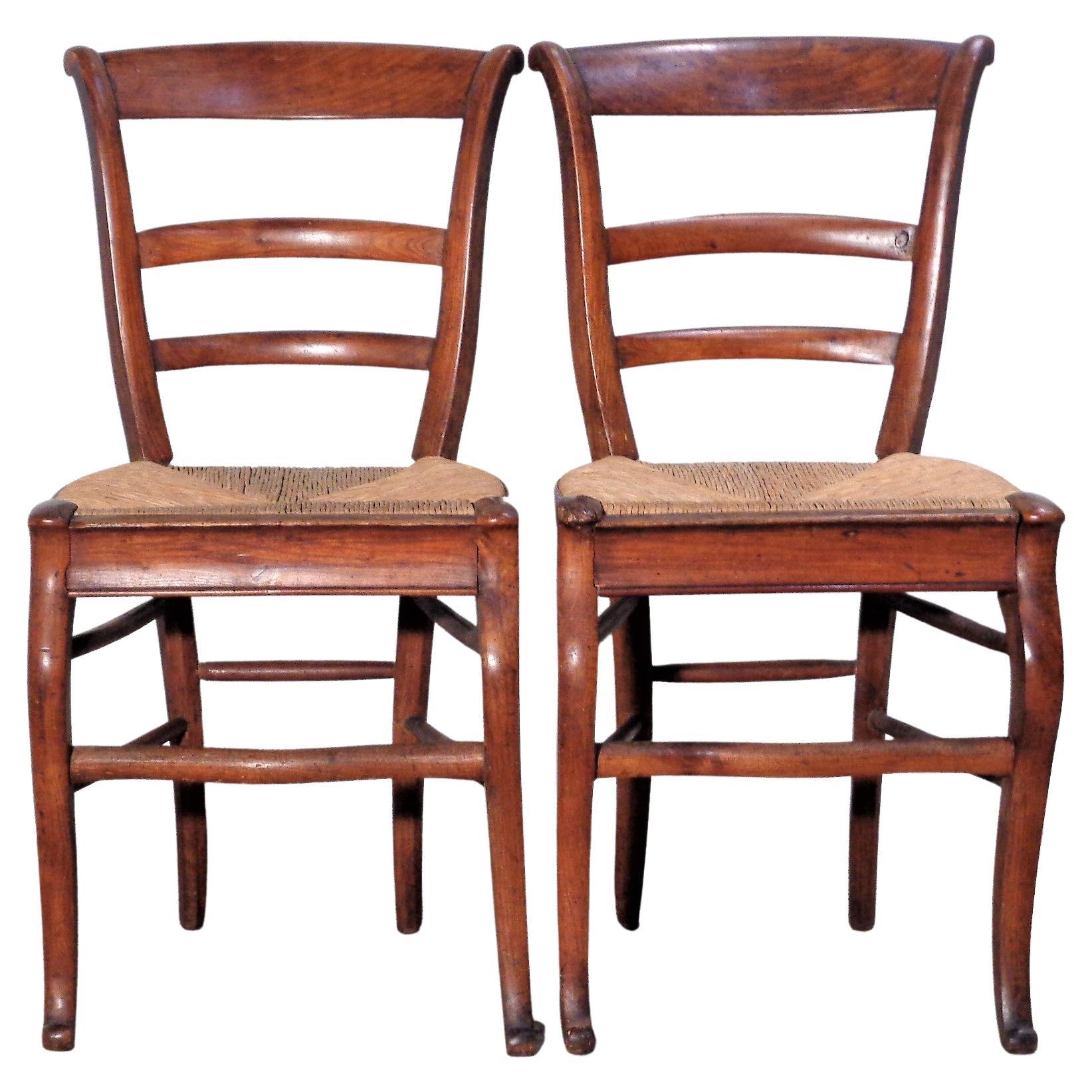 A matched pair of antique country French fruitwood chairs. Finely carved with a very unusual and exceptionally graceful sculptural form. Both chairs in beautifully aged original surface color patina w/ some small burled knots in wood. Date late 18th