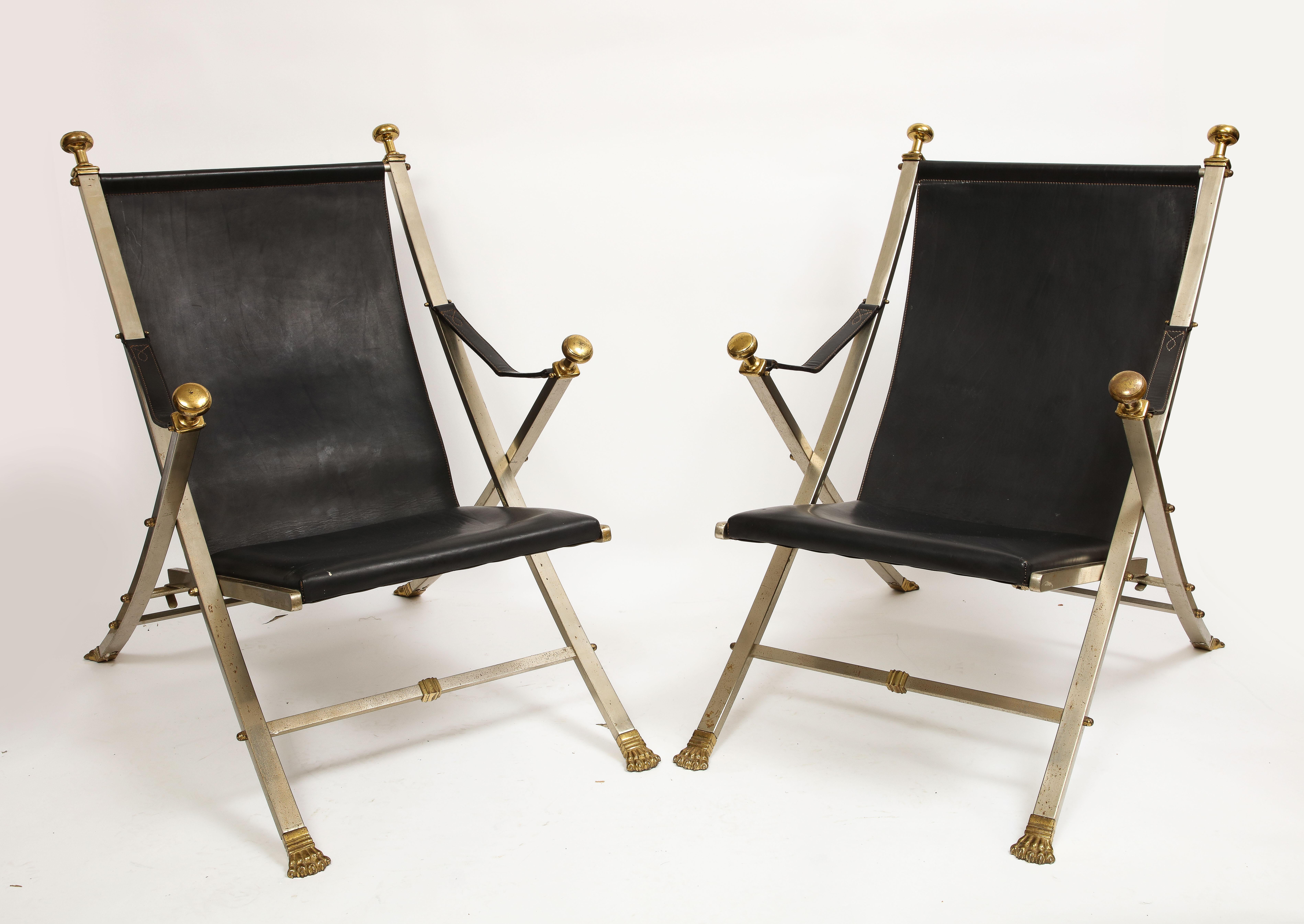A Rare and Unusual Pair of French Mid-Century Maison Jansen Polished Steel and Leather Folding Chairs. Each is hand-made with intricate detail and fantastic craftsmanship. They are made with black leather seats and straps and each is set in polished