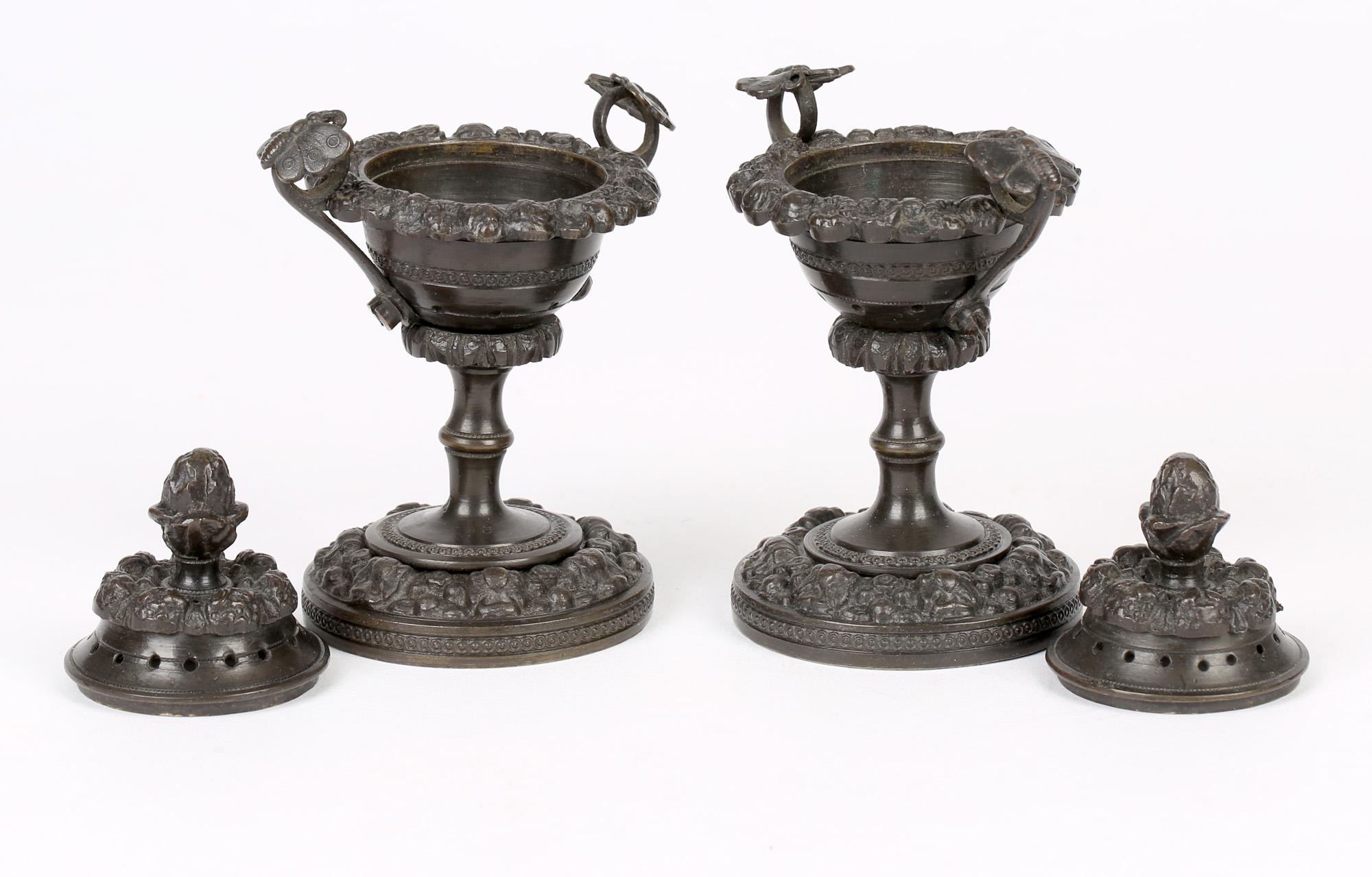 An unusual pair Georgian patinated bronze pot pourri vases and covers with butterfly mounted handles dating from around 1820. The vases stand on a wide rounded pedestal base relief moulded with floral designs with a narrow column stem with a bowl