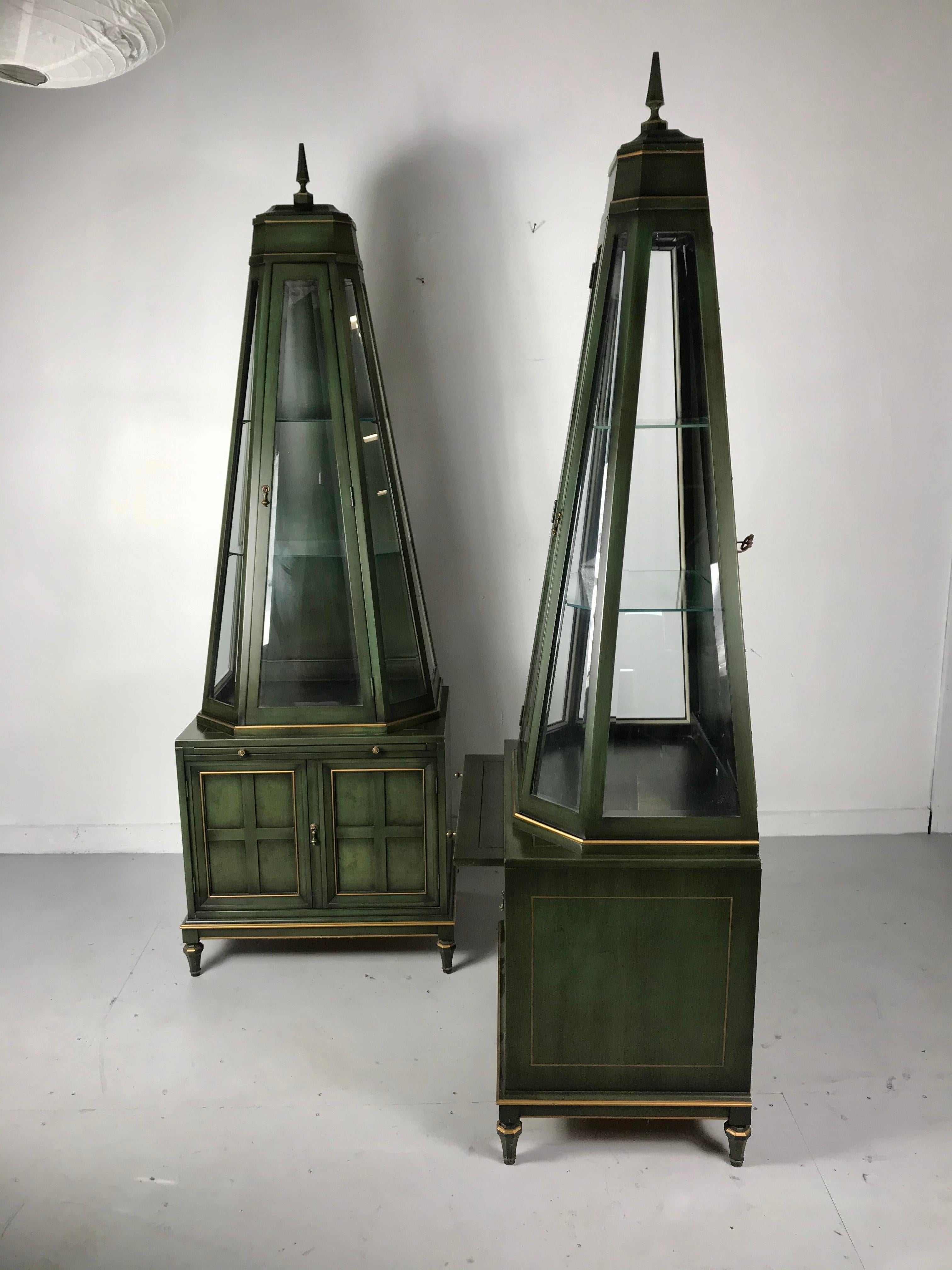 Unusual and stunning pair of decorative pyramidal curio cabinets, vitrines by Union National, beautiful hunter green with gold highlights, brass hardware and 3-sided beveled glass, triangle shape door, atop lower two-door cabinet and pull out /