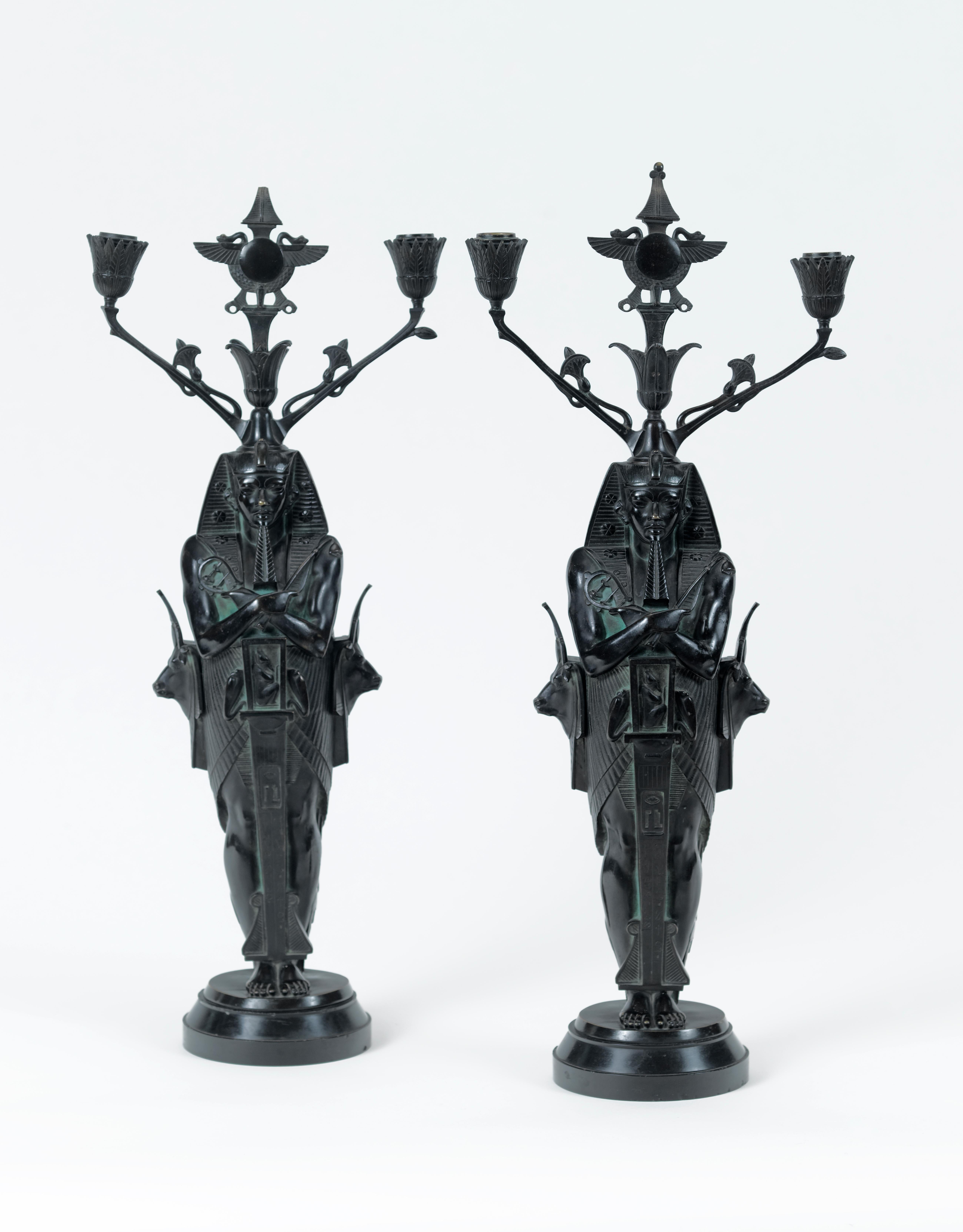 A very decorative pair of Egyptian revival patinated bronze candelabra, modelled as a pharoah supporting the central Egyptian symbol of Re, a sun disk, laterally two arms decorated with stylized lotus leaves, supporting cone-shaped nozzles, the back