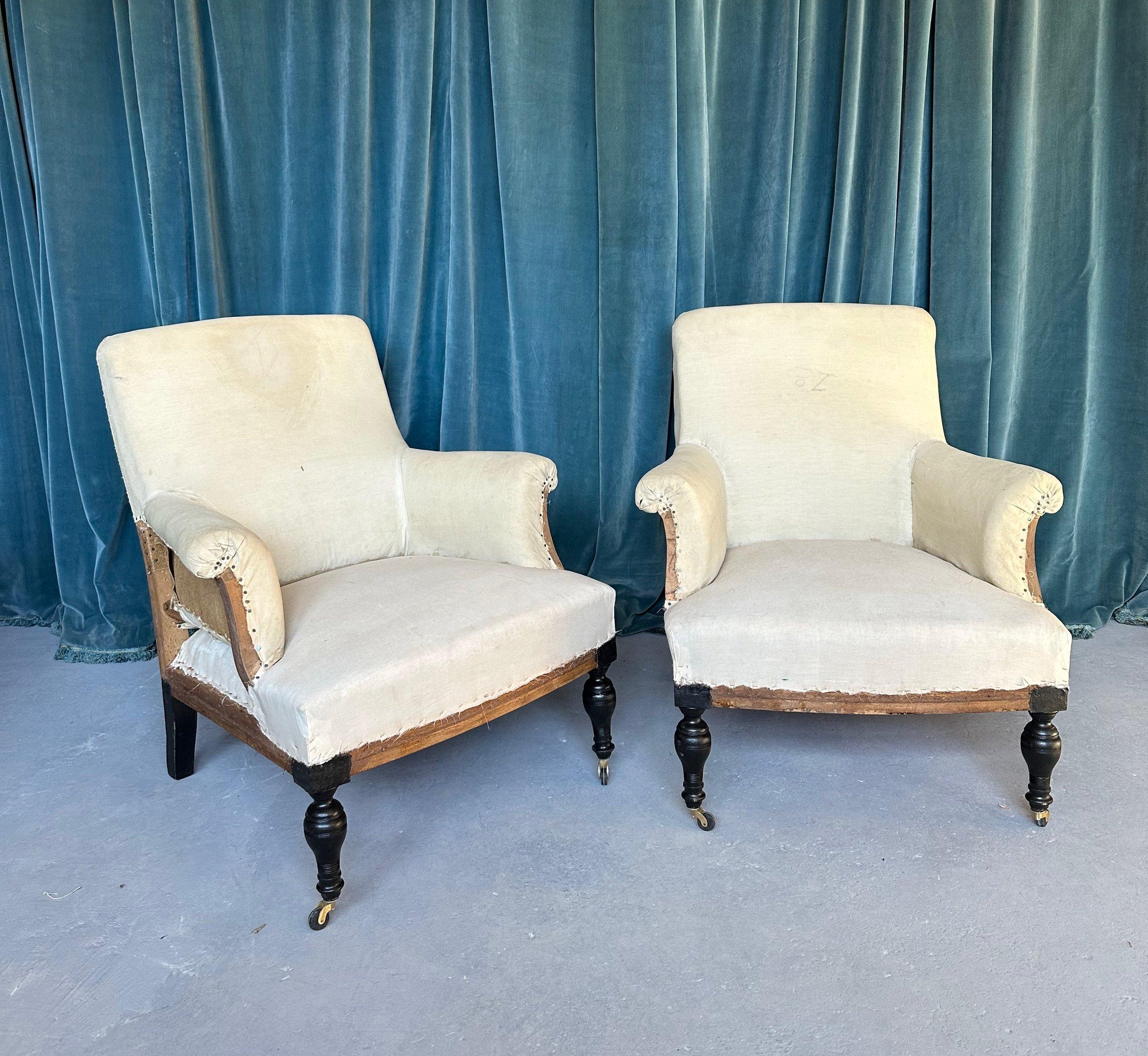 A very unique pair of French 19th century armchairs with straight untufted backs and scrolled arms, and simple untufted seats. The armchairs have unusual turned legs that have been recently fitted with new casters to accentuate the pitch and to make