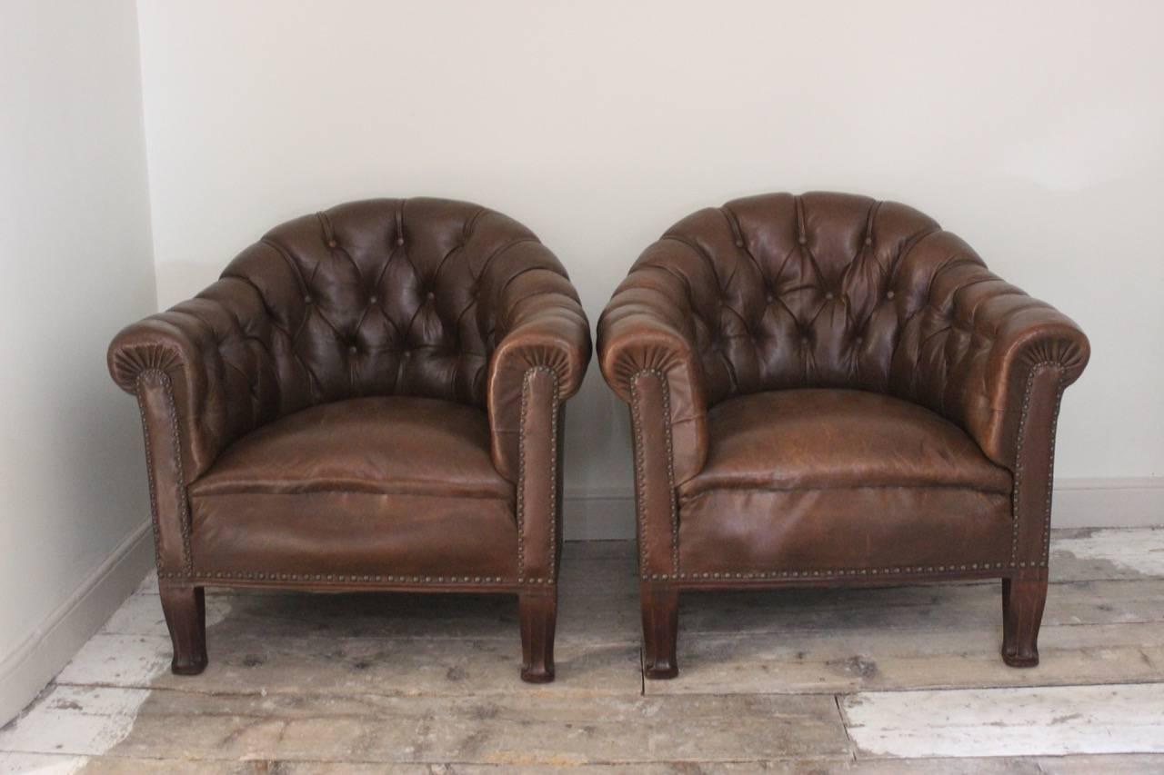 A good quality and of unusual design, pair of early to mid-20th century buttoned leather armchairs with shaped backs and Art Nouveau style carved feet 

Seat Height: 46cm.