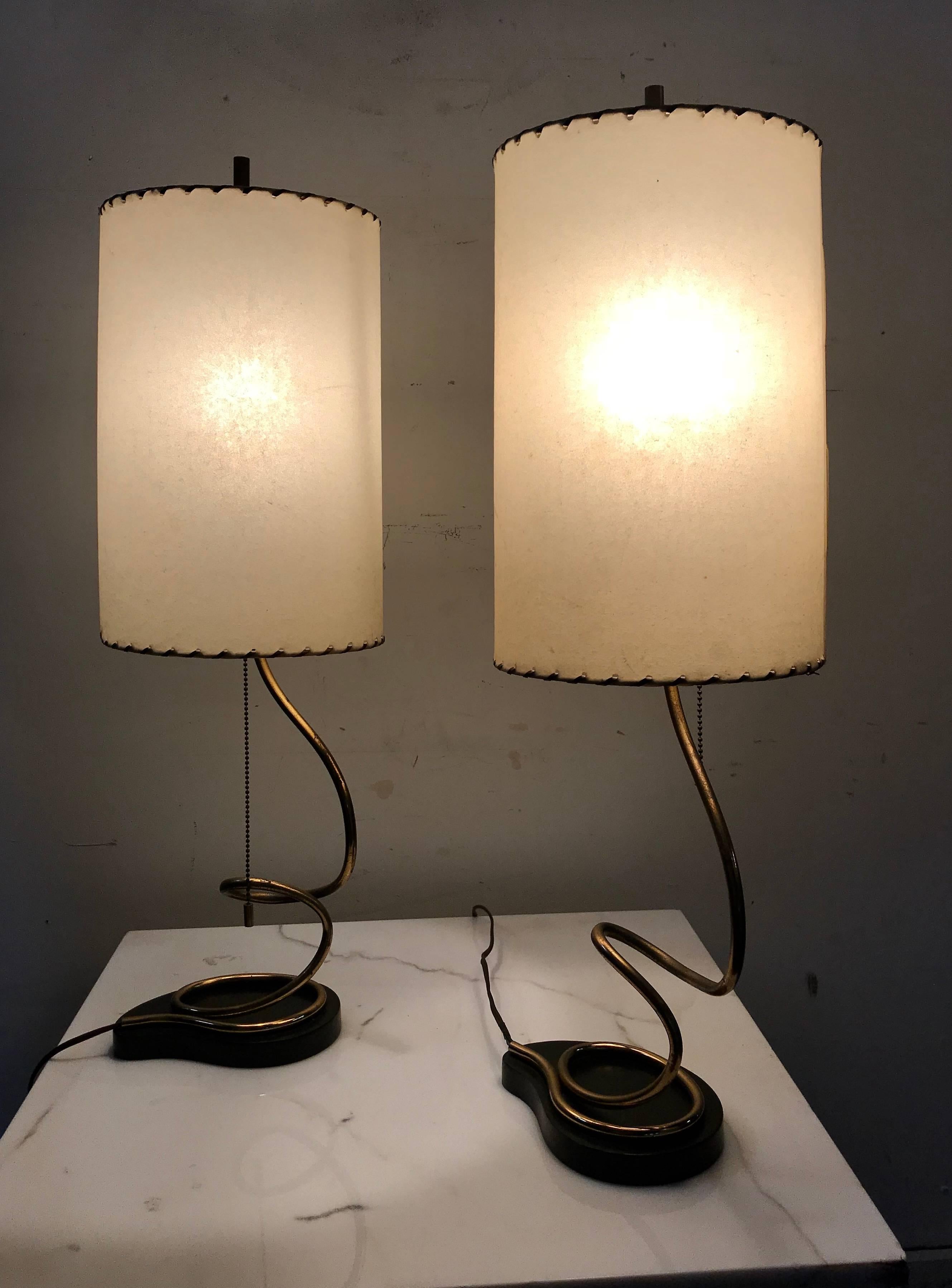 Unusual pair of majestic brass, metal and parchment table lamps. Lacquered metal kidney base with simple brass snake form standard, retain original cylinder parchment lamp shades.