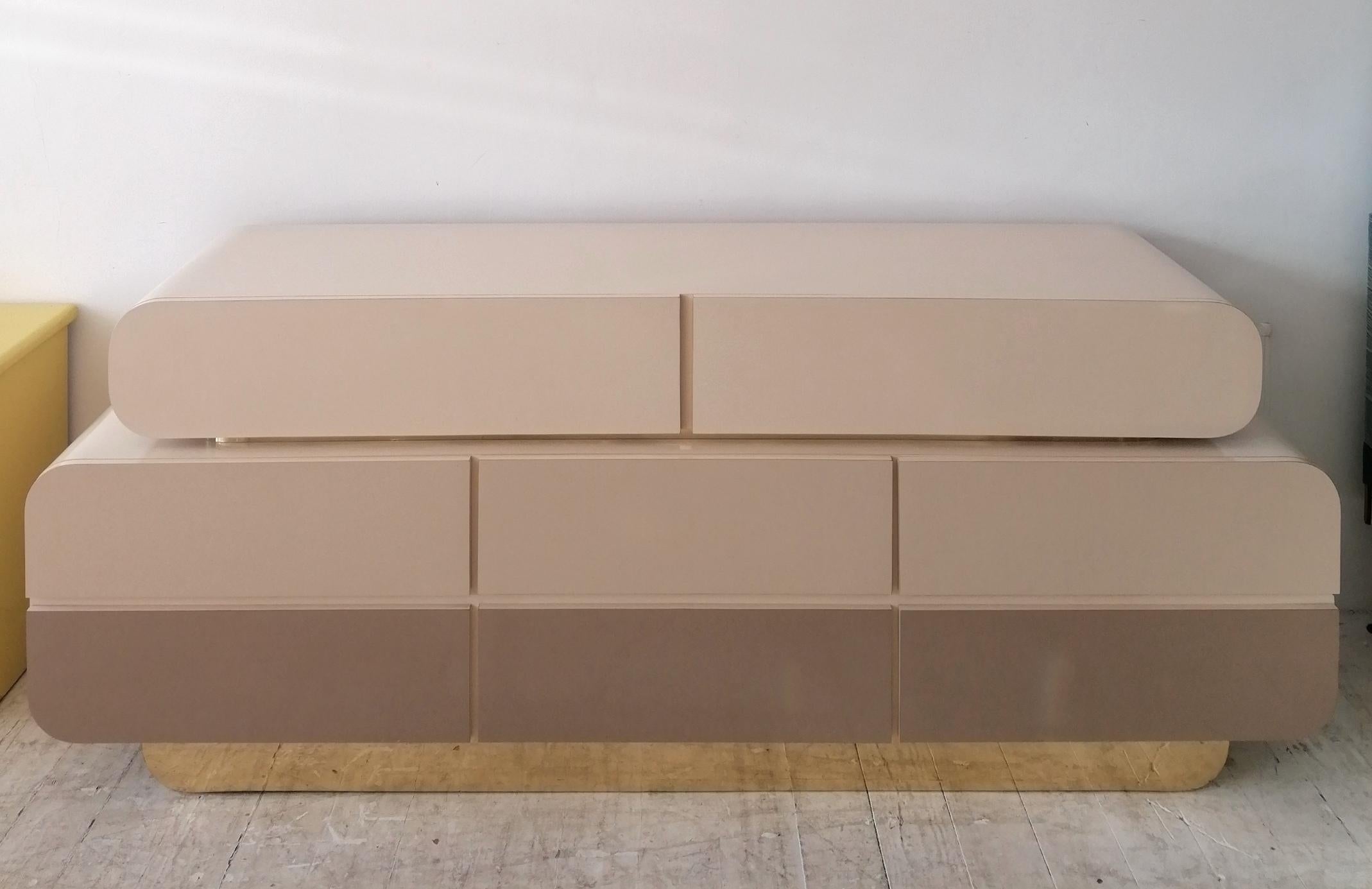 Buffet / buffet postmoderne inhabituel en forme de double cascade avec 8 tiroirs. La finition stratifiée est dans une palette neutre graduée : blanc cassé, beige et taupe, soulignée par une garniture en métal doré et un socle en métal doré. Une