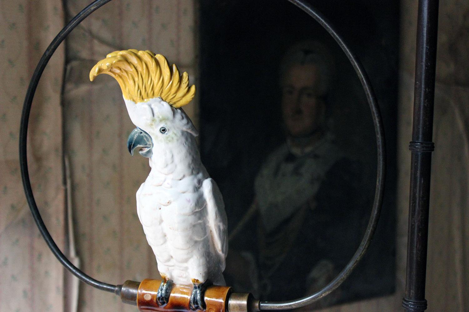 The large floor standing frame, fitted with a late 19th century porcelain Dresden(?) sulphur crested cockatoo, the bird perched within a swinging brass hoop, within an Edwardian period upper frame with finial, the lower Regency period base having a