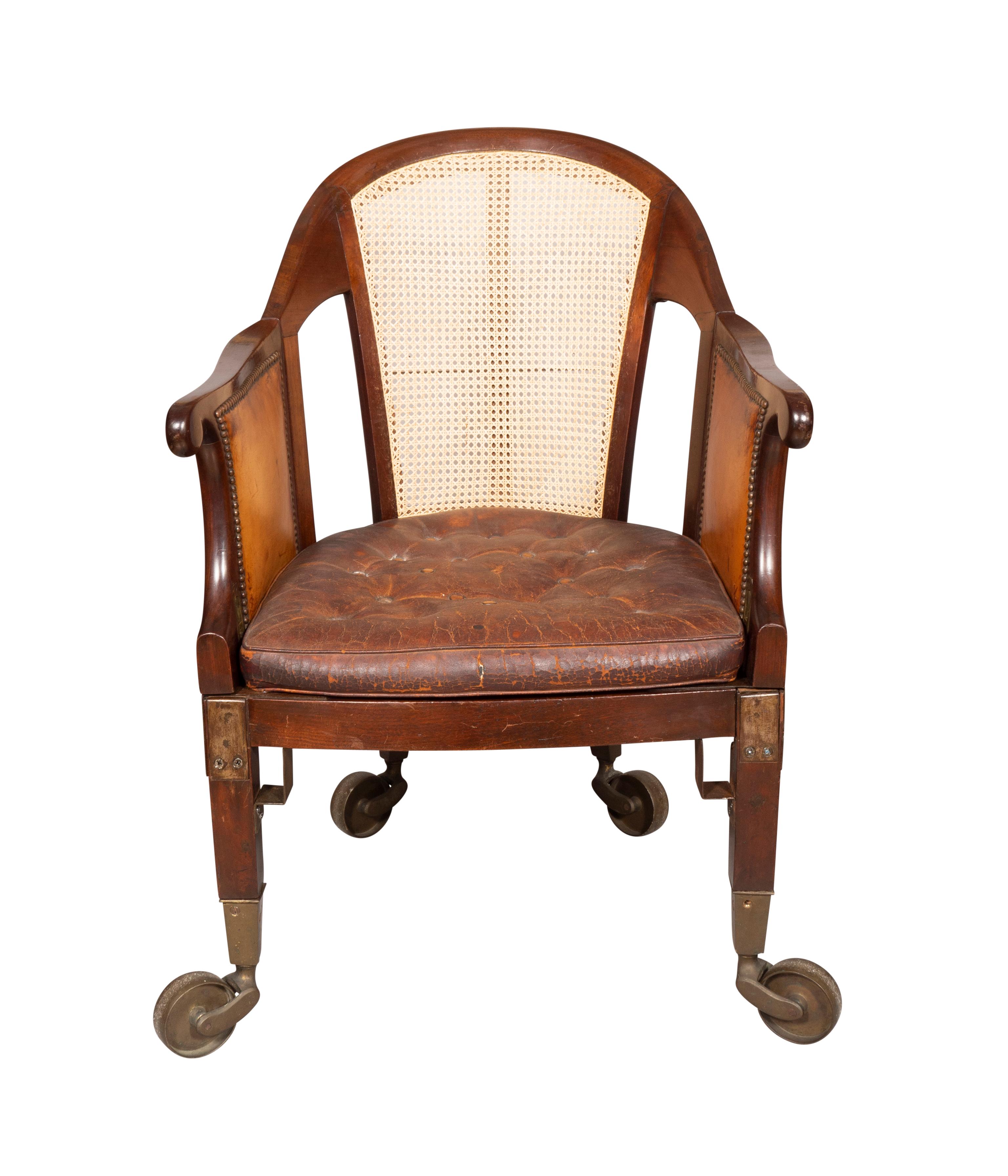 An unusual chair with arched back newly caned. The sides newly caned and the sides swing open to access easily. Raised on square section legs and very large brass casters .Leather cushion seat and sides.