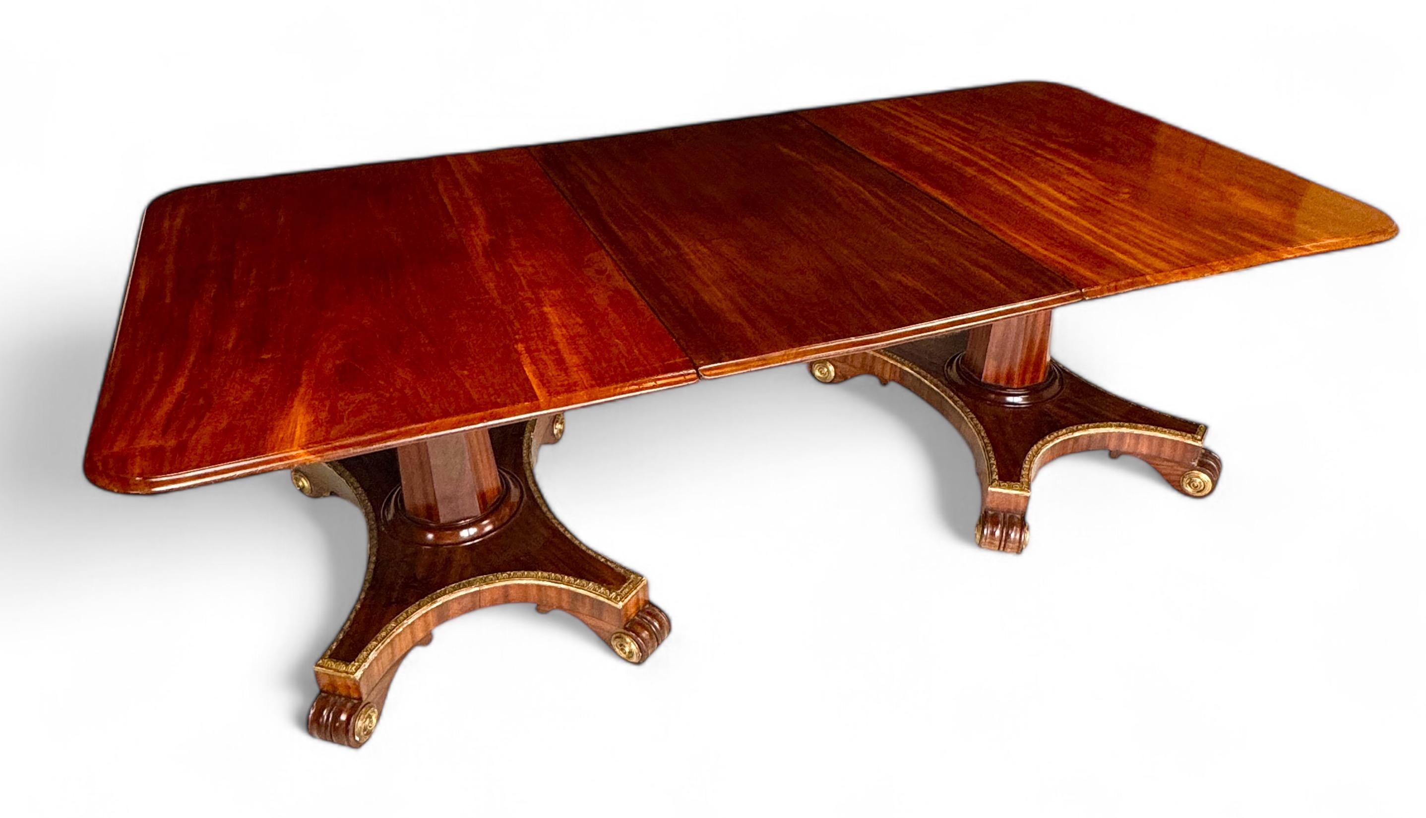 Unusual Regency twin pedestal mahogany and parcel gilt dining table
In the manner of Morel & Seddon, the rounded rectangular moulded tilting tops, with narrow ends to create two breakfast tables together with an additional central leaf; on octagonal