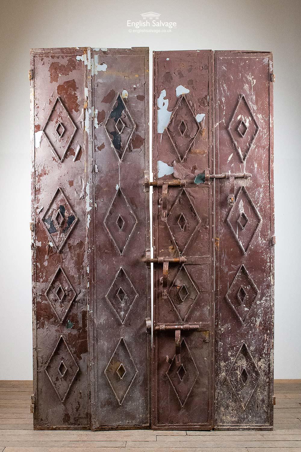 Set of sheet metal folding doors from a Moroccan film set. Each door is 36cm wide. Painted brown to the one side with diamond and circle detailing and three large bolts. The rear sides have a large harlequin like brown and white design. Four doors