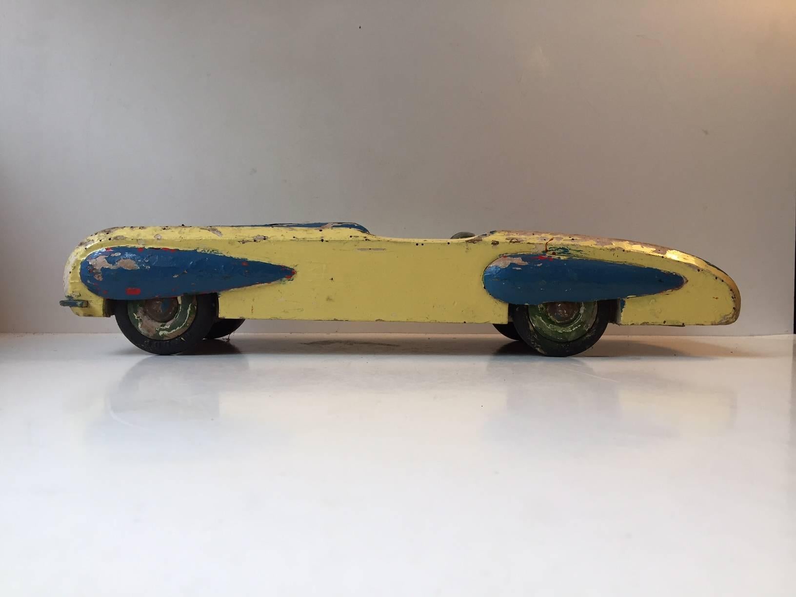 Grande voiture jouet en bois peint avec beaucoup d'articles et de personnalité. Nombreux trous de vers, plusieurs zones où la peinture s'est usée, beaucoup de rayures et d'éraflures, tout autour. Bien qu'elle soit montée avec des pneus Dunlop, cette