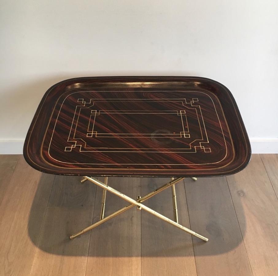 This tray table is made of a folding brass base with a lacquer tole top with gilt geometrical decor. This is a French work, circa 1950.
