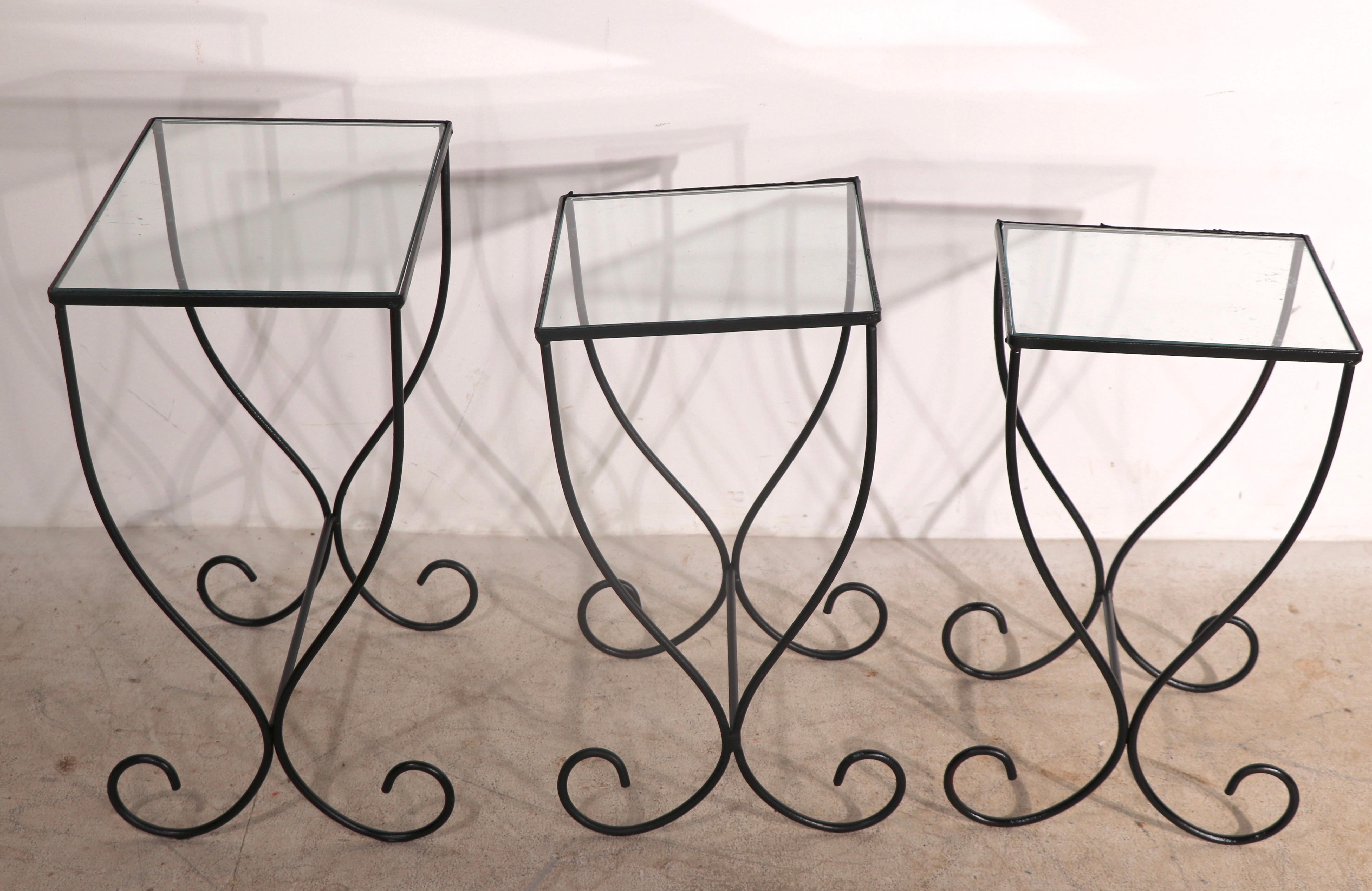 Unusual set of three wrought iron and glass nesting tables, having curlicue scroll legs, wrought iron frames with glass tops. The three graduated tables nest into the larger table. We believe these are American made Mid 20th C. The tables are