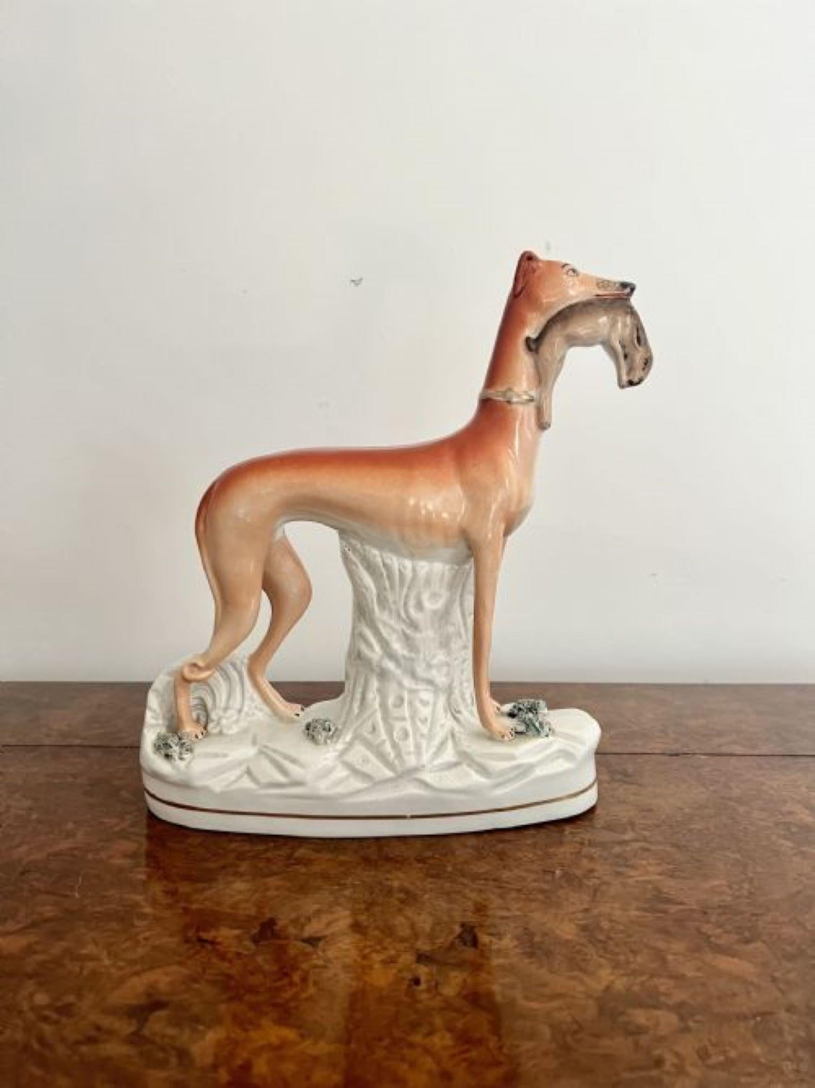 Unusually large antique Victorian staffordshire greyhound figure having an unusually large antique Victorian Staffordshire greyhound figure holding a rabbit in its mouth, hand painted in white and brown colours, standing on an oval gilded shaped