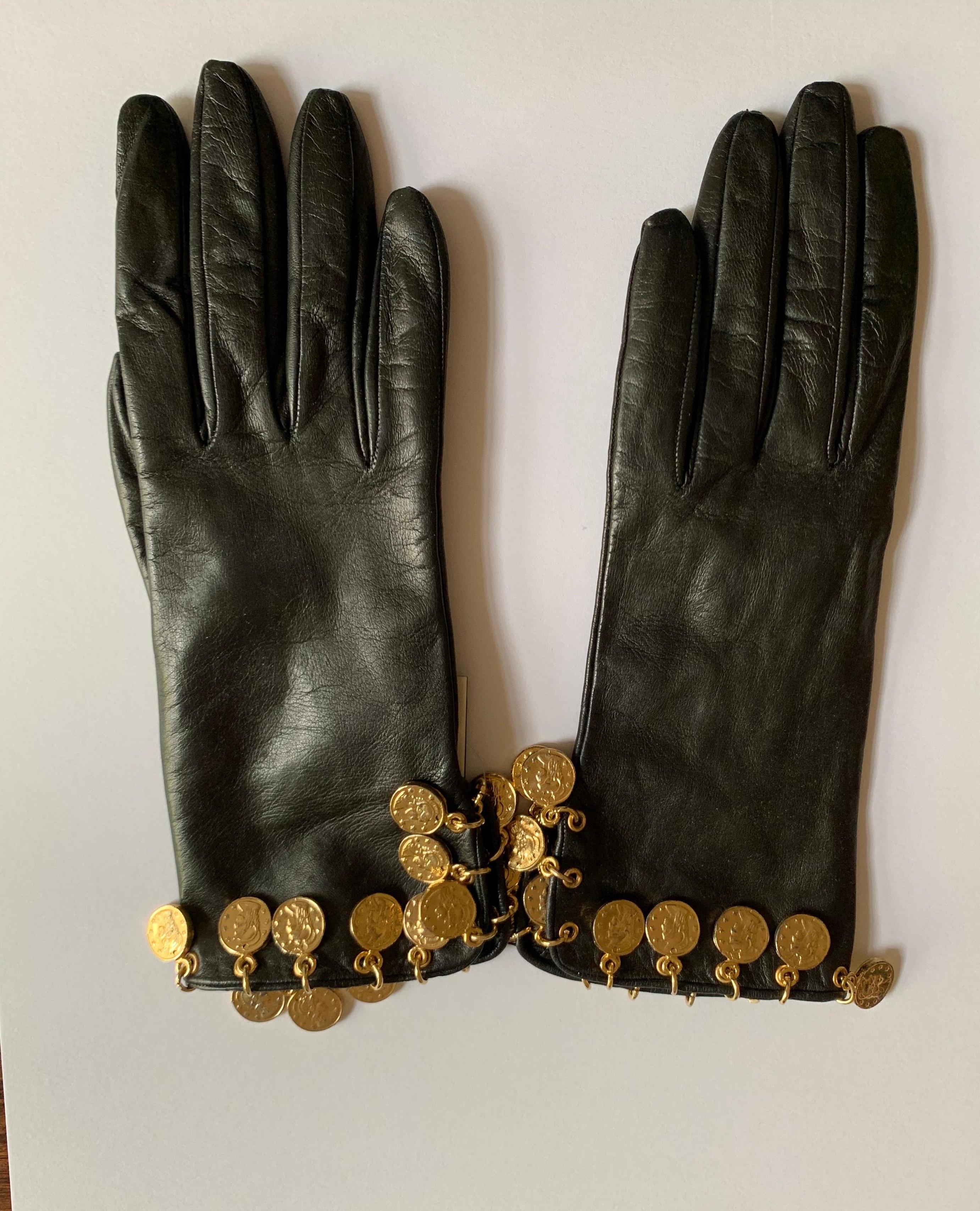 Vintage Moschino black leather gloves with cuffs adorned with dangling Roman coin inspired gold tone charms. 

Leather, lined in silk. 

Made in Italy.

Size 7 1/2, best fits small.

Very good condition, unworn with tags still attached, faint