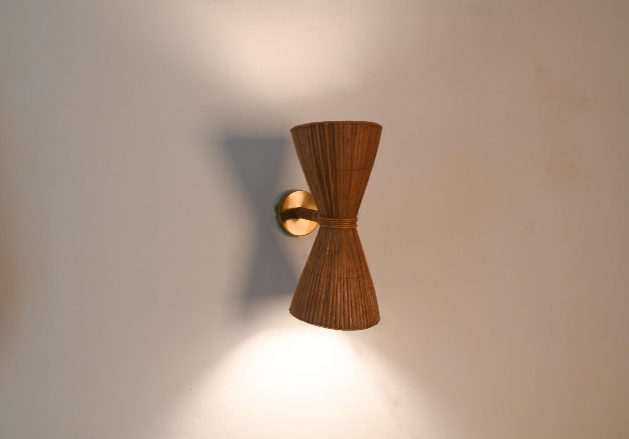 Prova l'eleganza e le vibrazioni moderne con la nostra lampada da parete Up & Up in rattan. Realizzata a mano in rattan di canna da zucchero, questa lampada a forma di cono presenta un design verticale e un accento dorato. Cablata per una finitura