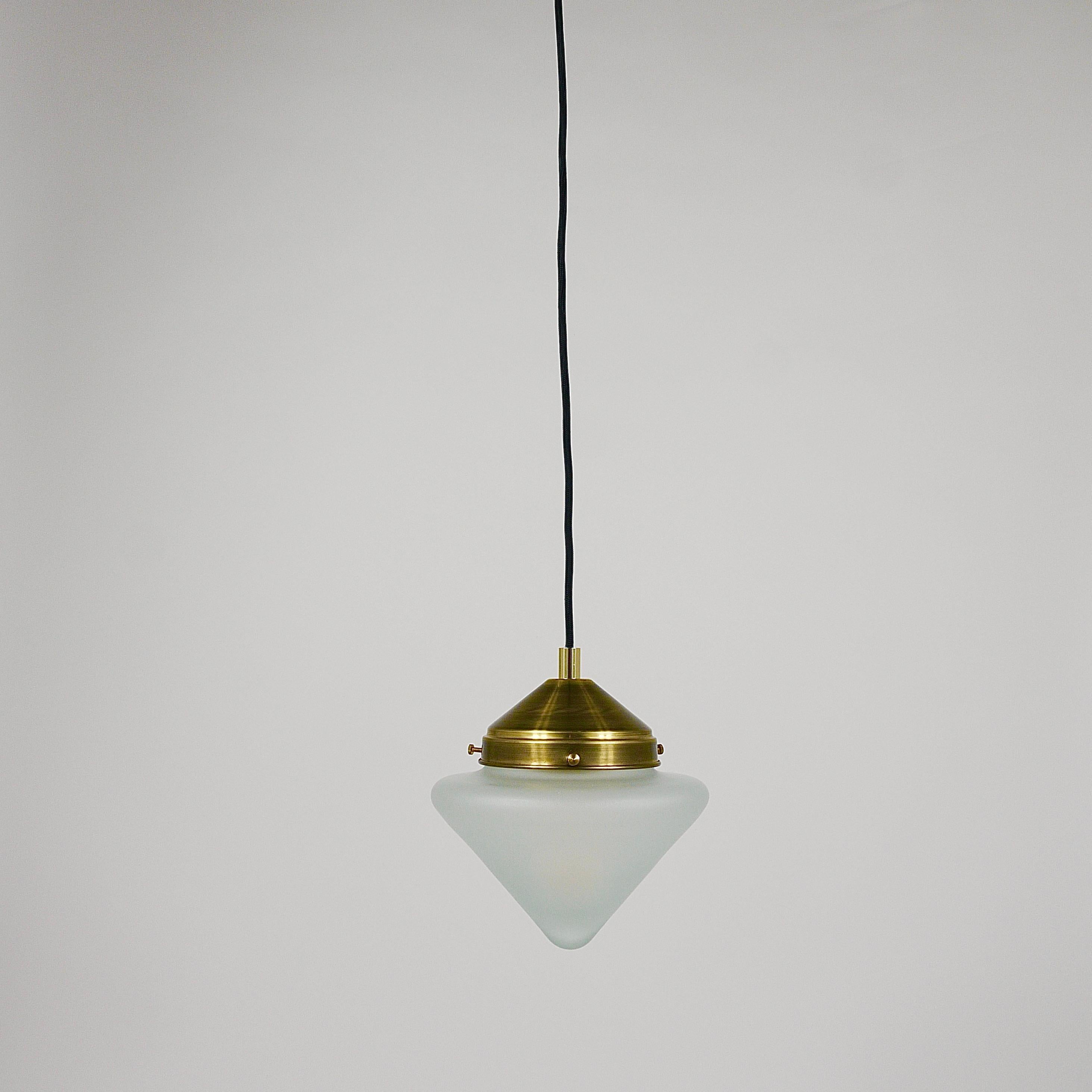Up to 10 Art Deco Schoolhouse petite pendant lights / hanging lamps from the 1930s, crafted in Vienna, Austria. These lights feature brass hardware with the original beautifully shaped conical satin glass lampshades. Ten pieces are available, sold